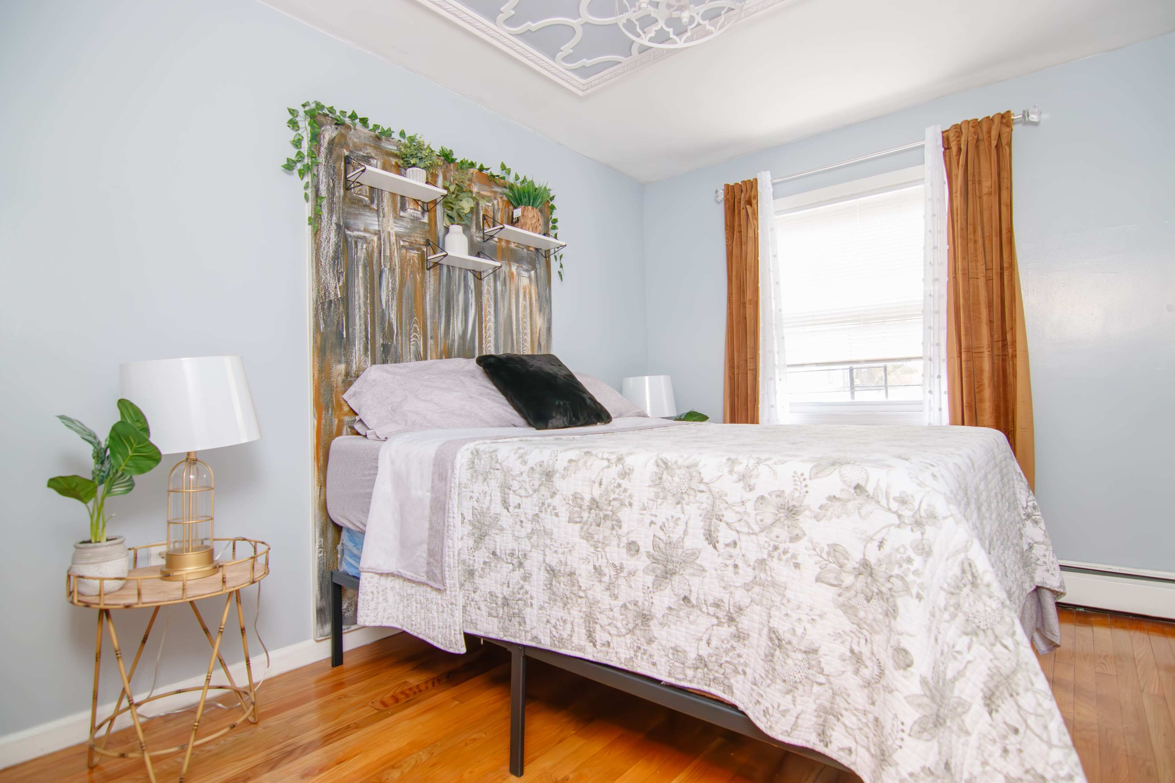 A neatly arranged bedroom with a bed, two lamps, a decorative headboard made of metal, and indoor plants.