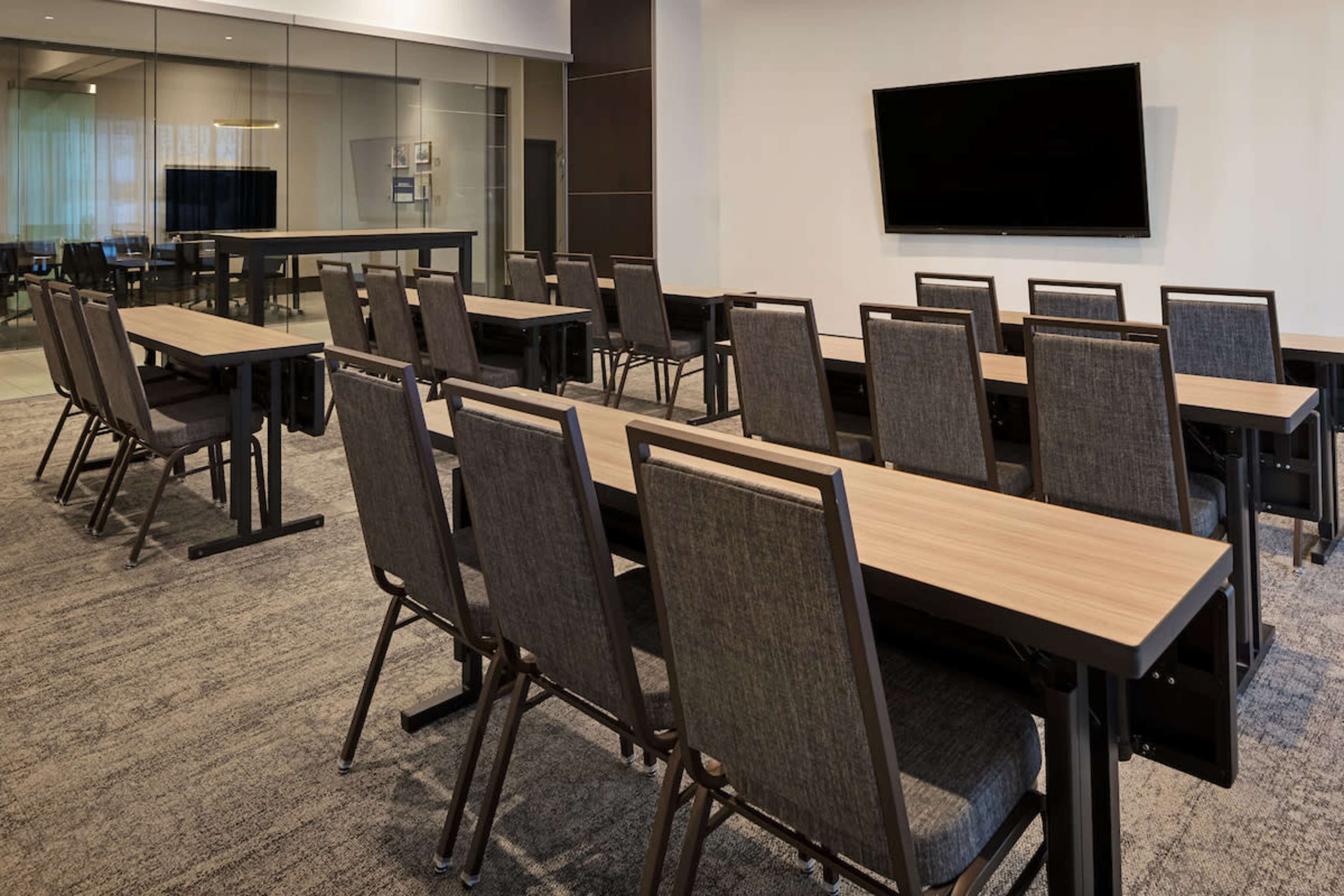 The image shows a conference room with several tables arranged in a row and chairs facing a wall-mounted television.