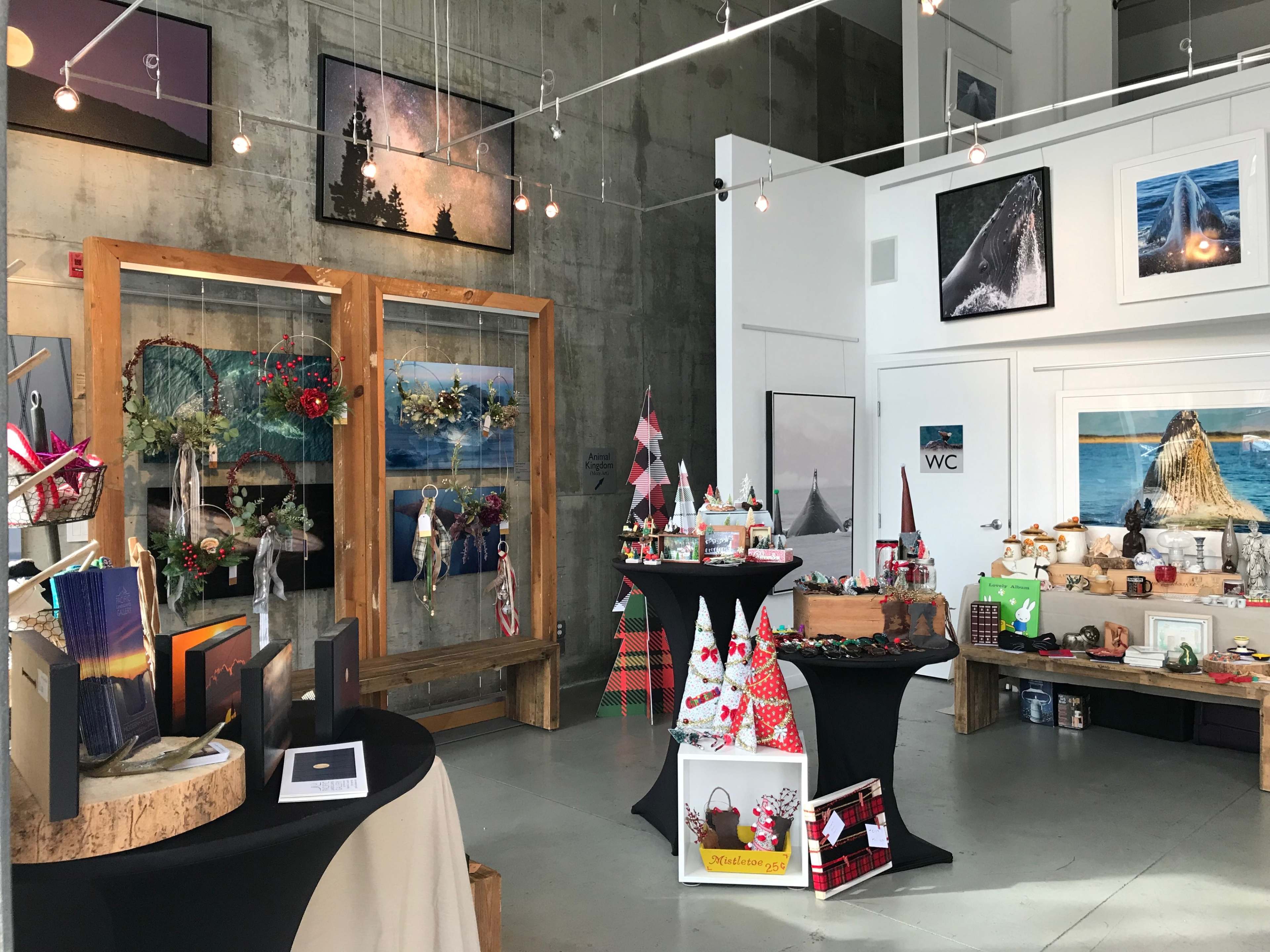 An art gallery featuring various displays of crafts, photographs, and holiday decorations arranged around the room.