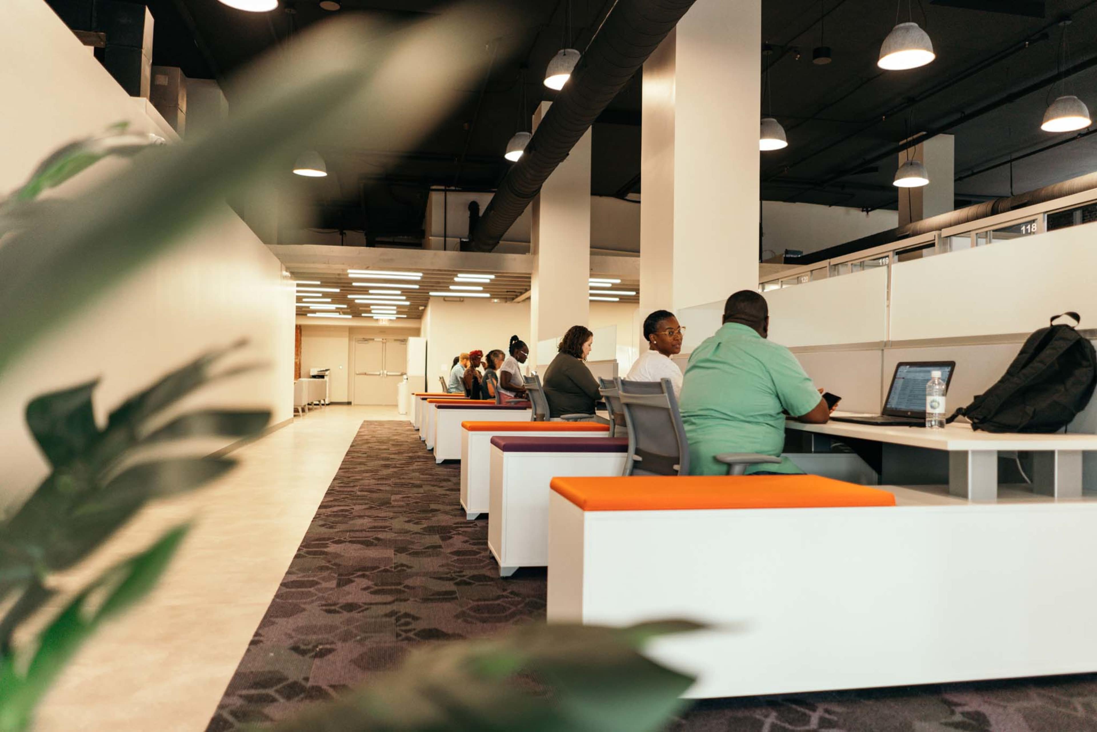 The image shows several people working at individual desks in a modern office space, with a focus on a bright, open design.