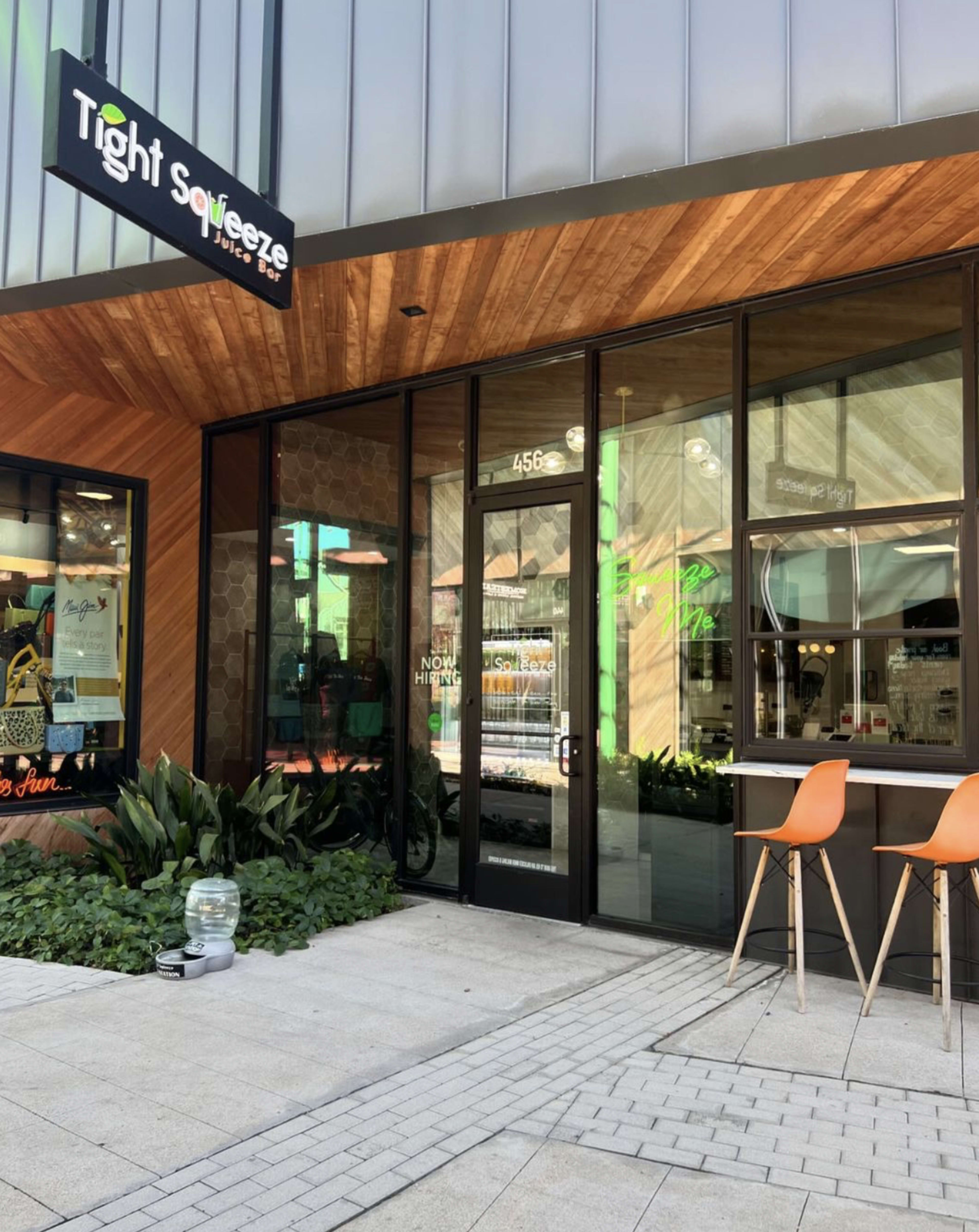 The image shows the entrance of a business named "Tight Squeeze" with large glass windows, a wooden accent wall, and outdoor seating.