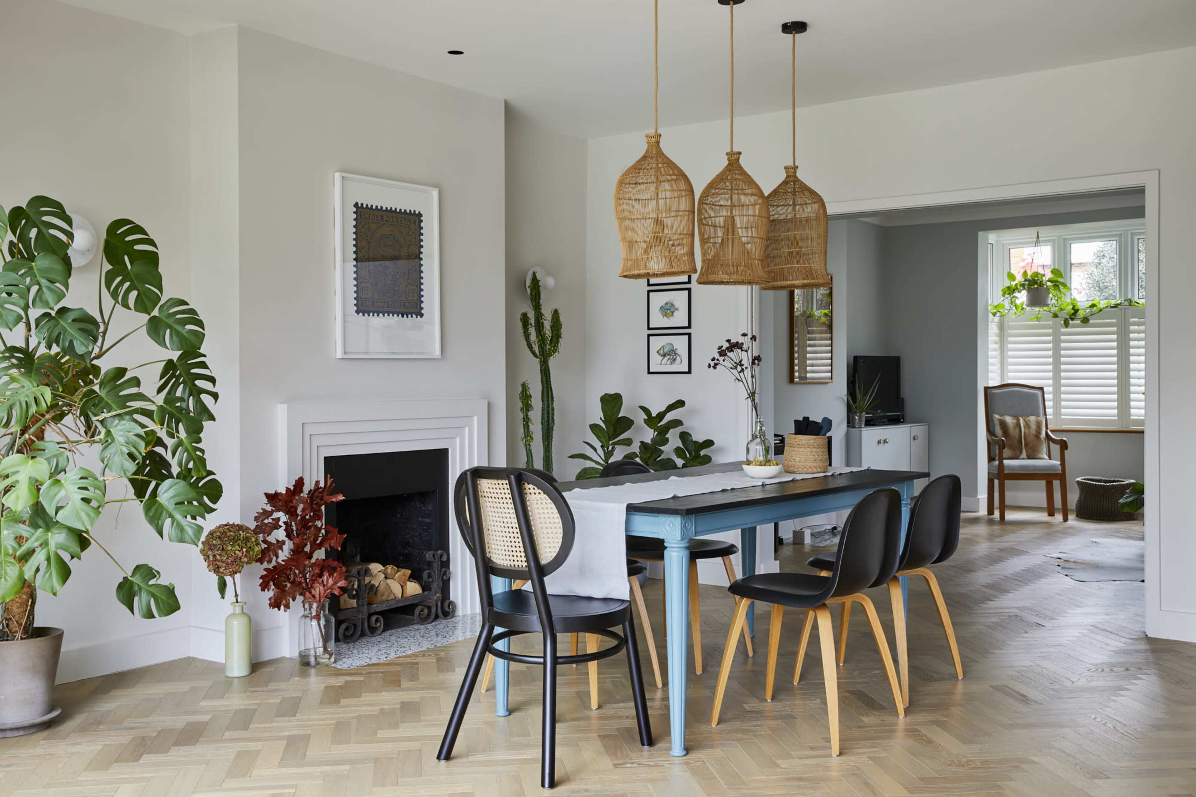 A modern dining area features a wooden table surrounded by black and natural woven chairs, with plants and decorative elements enhancing the space.