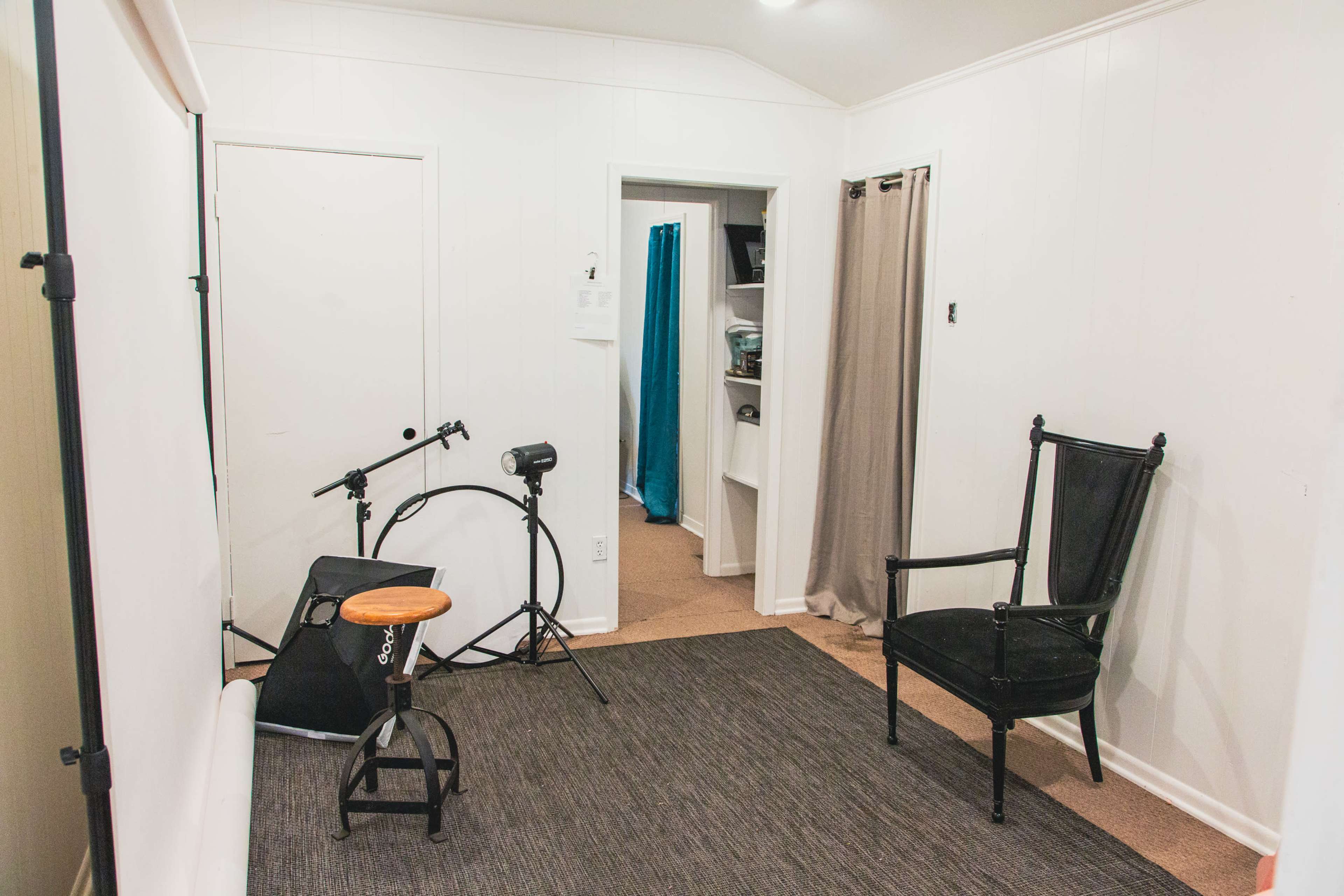 A small room features a chair, a drum kit, a stool, and curtains, with a doorway leading to another area.