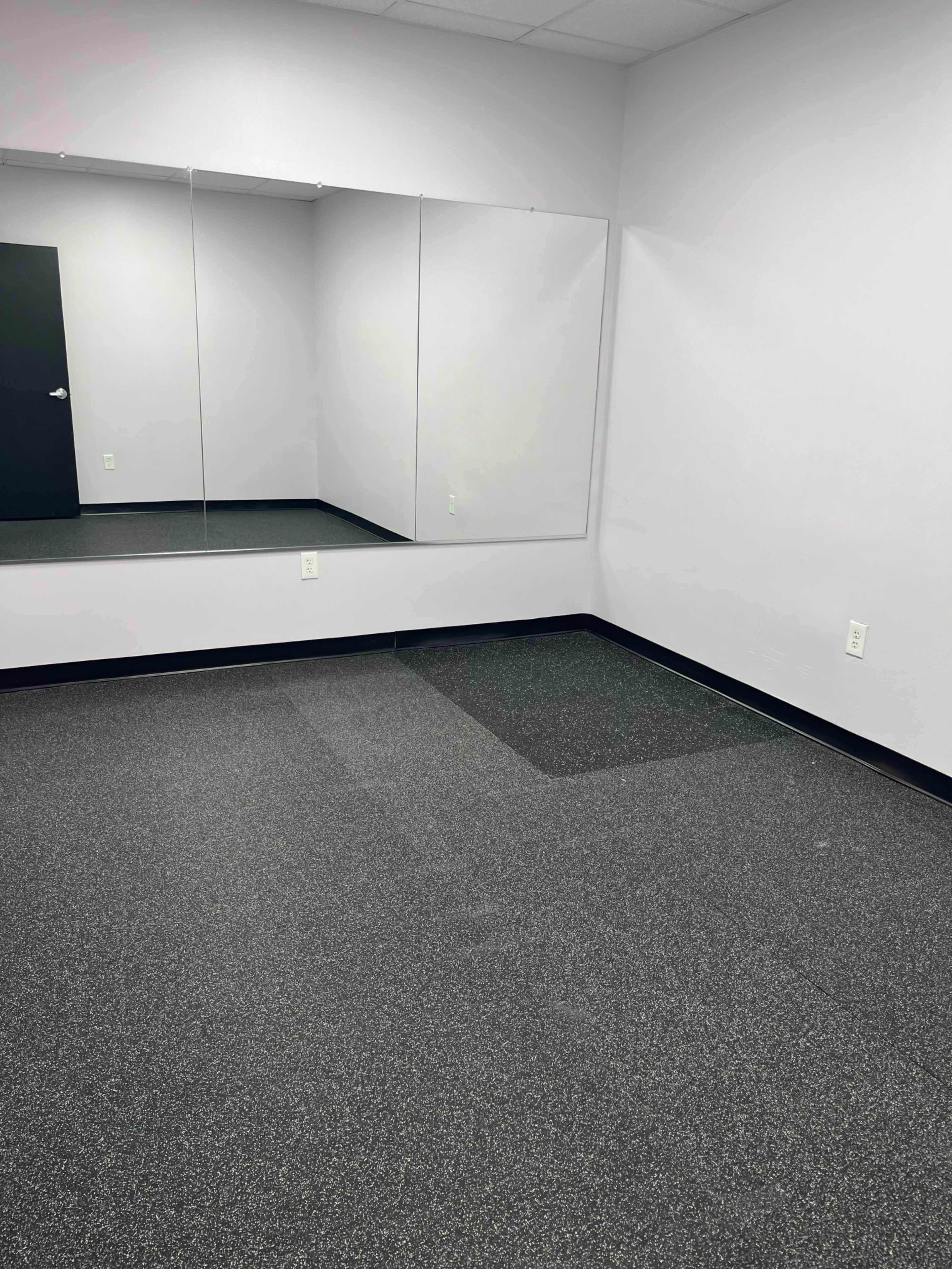 A sparsely furnished room with gray flooring and large mirrors on one wall.