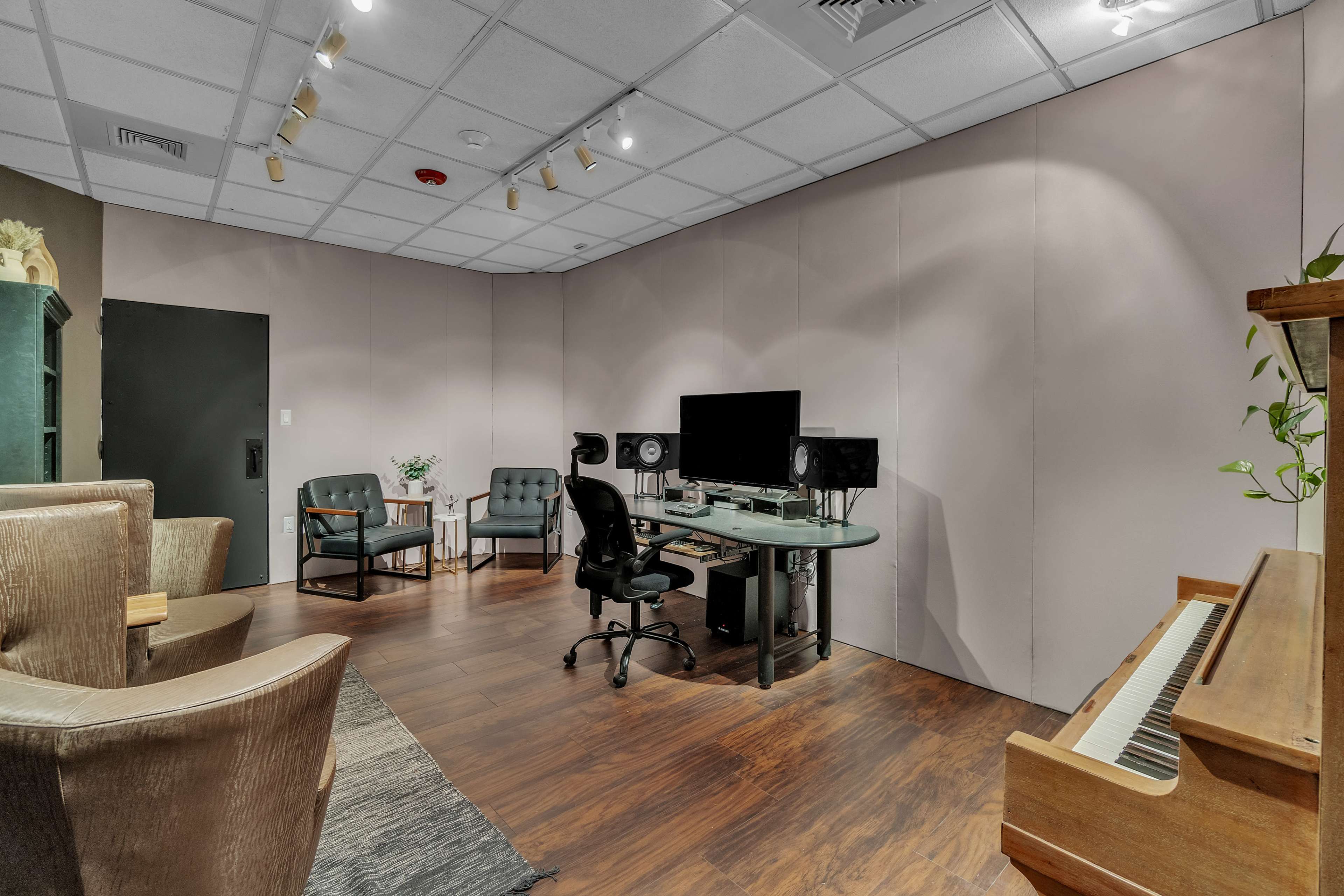 The image shows a recording studio with a music production setup, including a computer, speakers, and a piano, along with seating areas.