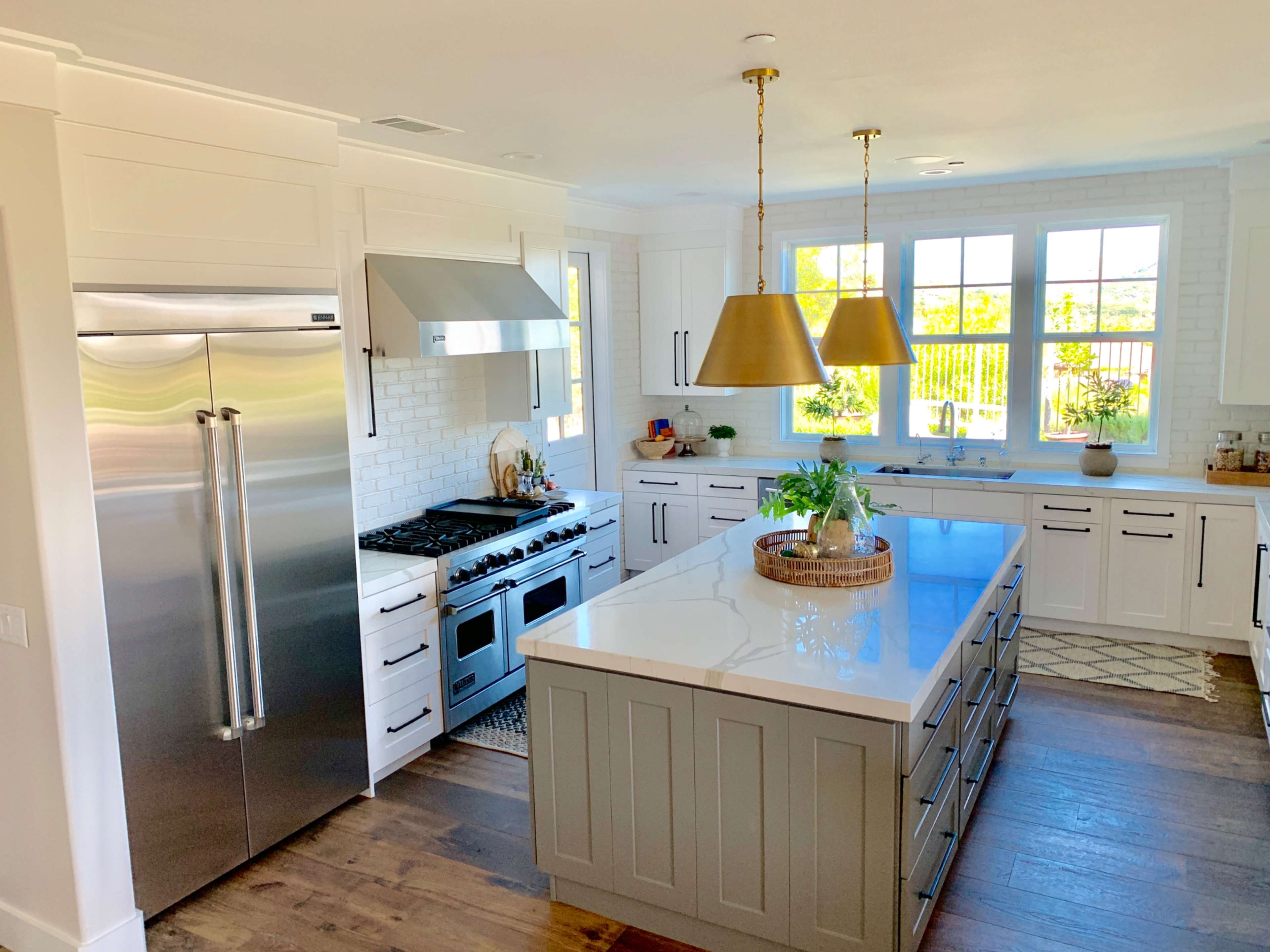 A modern kitchen features a large island with a white countertop, stainless steel appliances, and ample natural light from the windows.