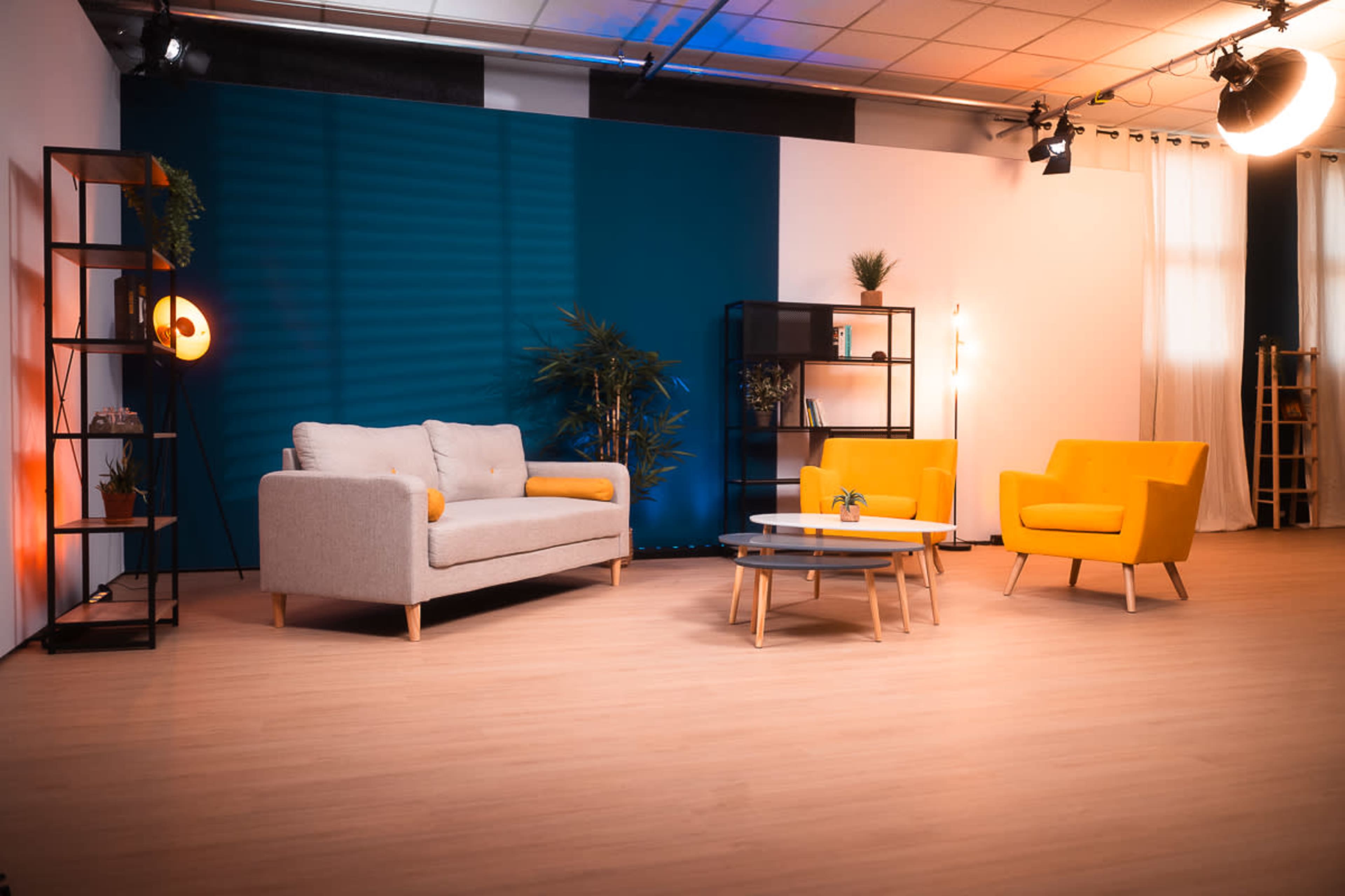A modern interior design setup with a gray sofa, two yellow armchairs, a coffee table, and shelving units against a backdrop of blue and white walls.