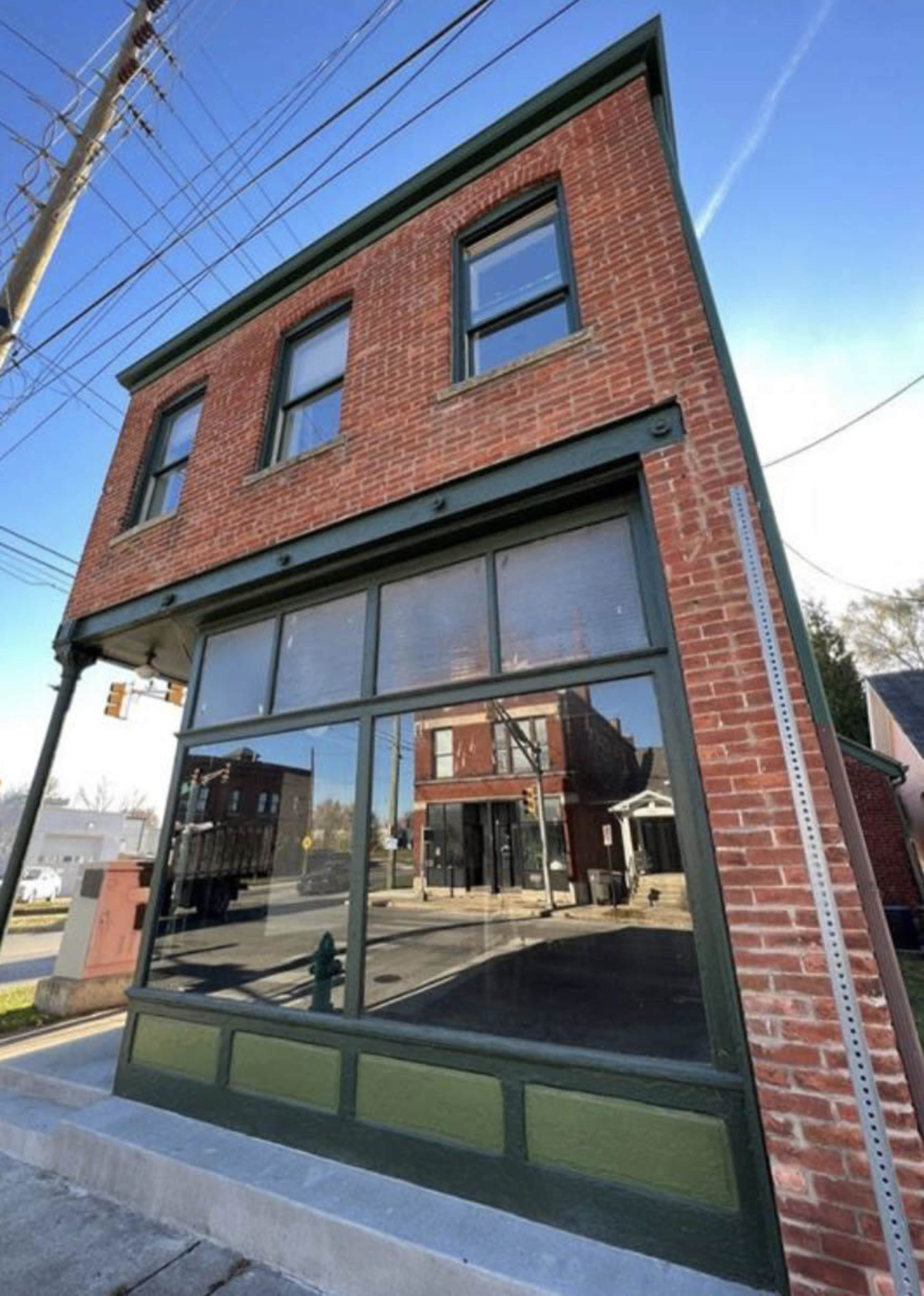 A brick building with large glass windows at a street corner, featuring a green trim and a clear blue sky above.