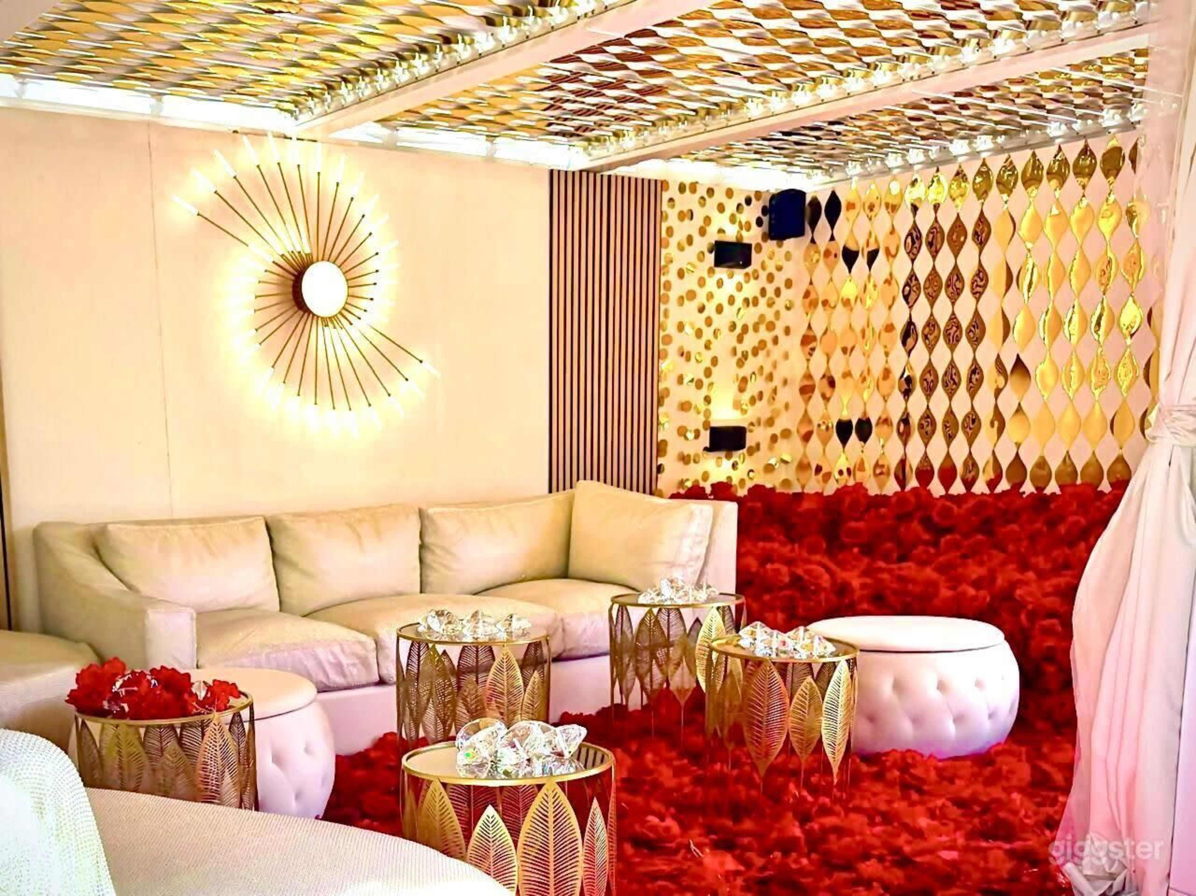 The image shows a stylish living room with a white sectional sofa, gold-accented tables, and a plush red carpet.