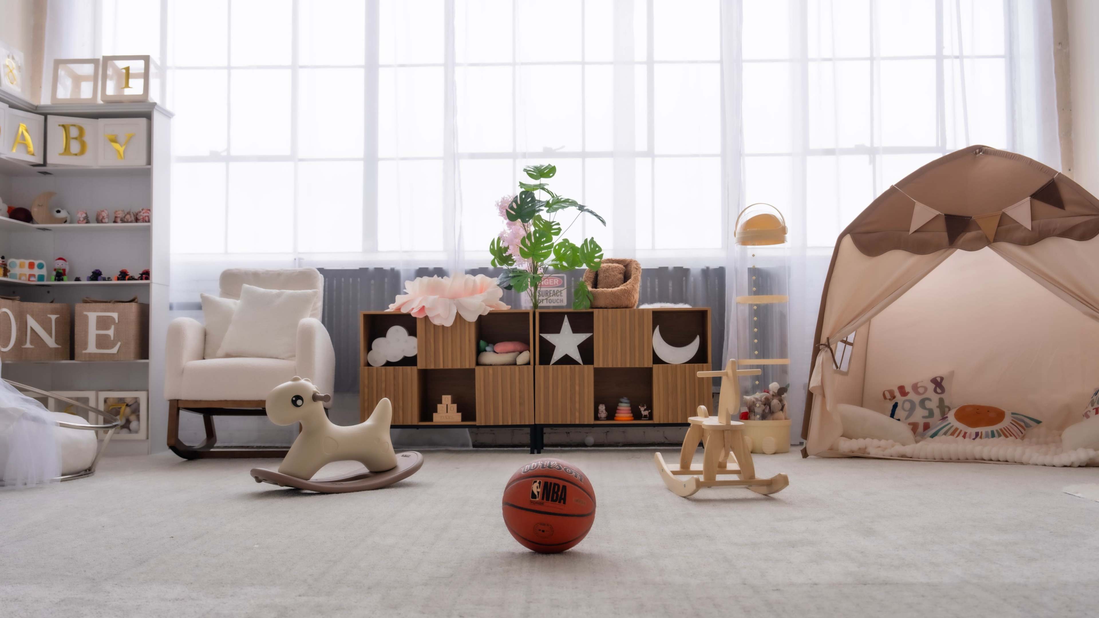The room features a cozy play area with a rocking dog, a basketball, and playful decor, including a wooden shelf and a tent.
