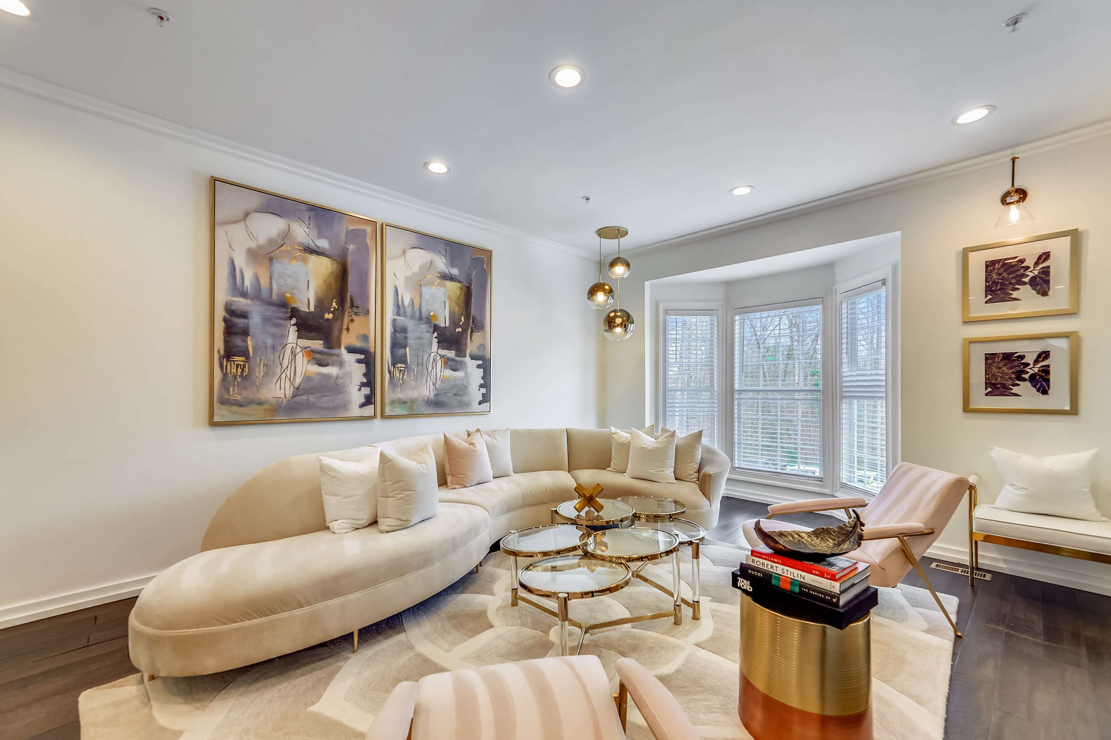 A modern living room features a curved beige sectional sofa, a glass coffee table, and large abstract paintings on the walls.