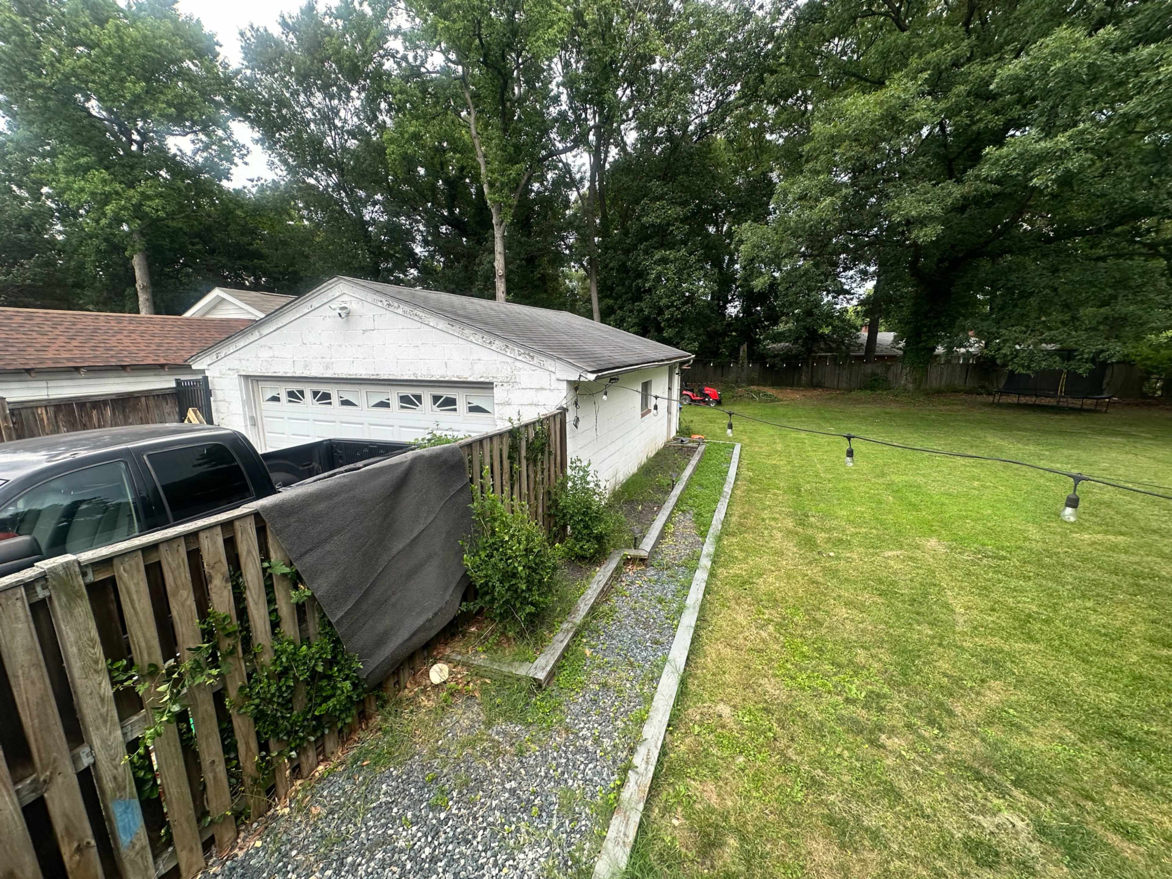 The image shows a white garage situated next to a gravel pathway and a fenced area in a grassy backyard.