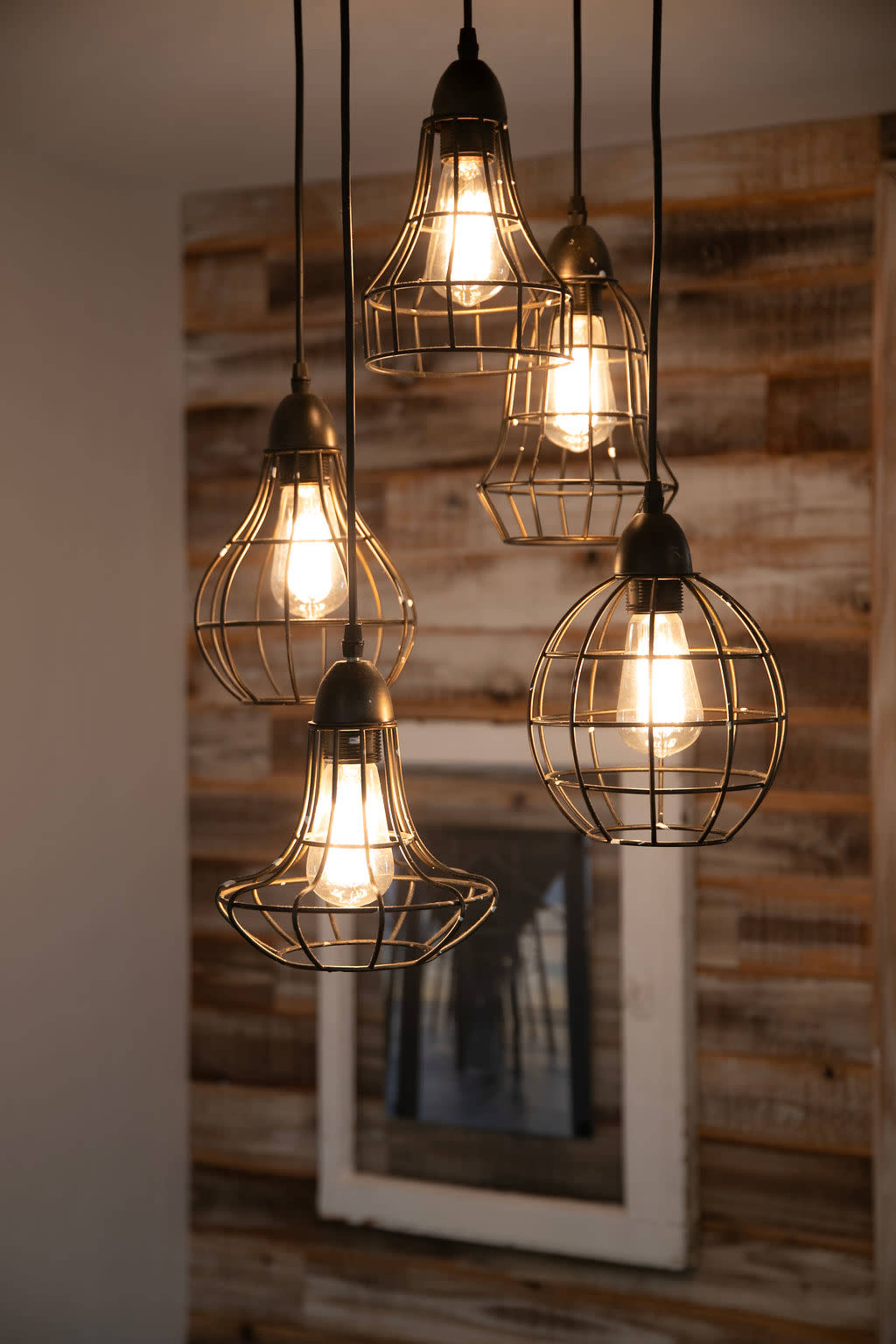A group of five vintage-style pendant lights with wire cages hangs against a backdrop of wooden paneling.