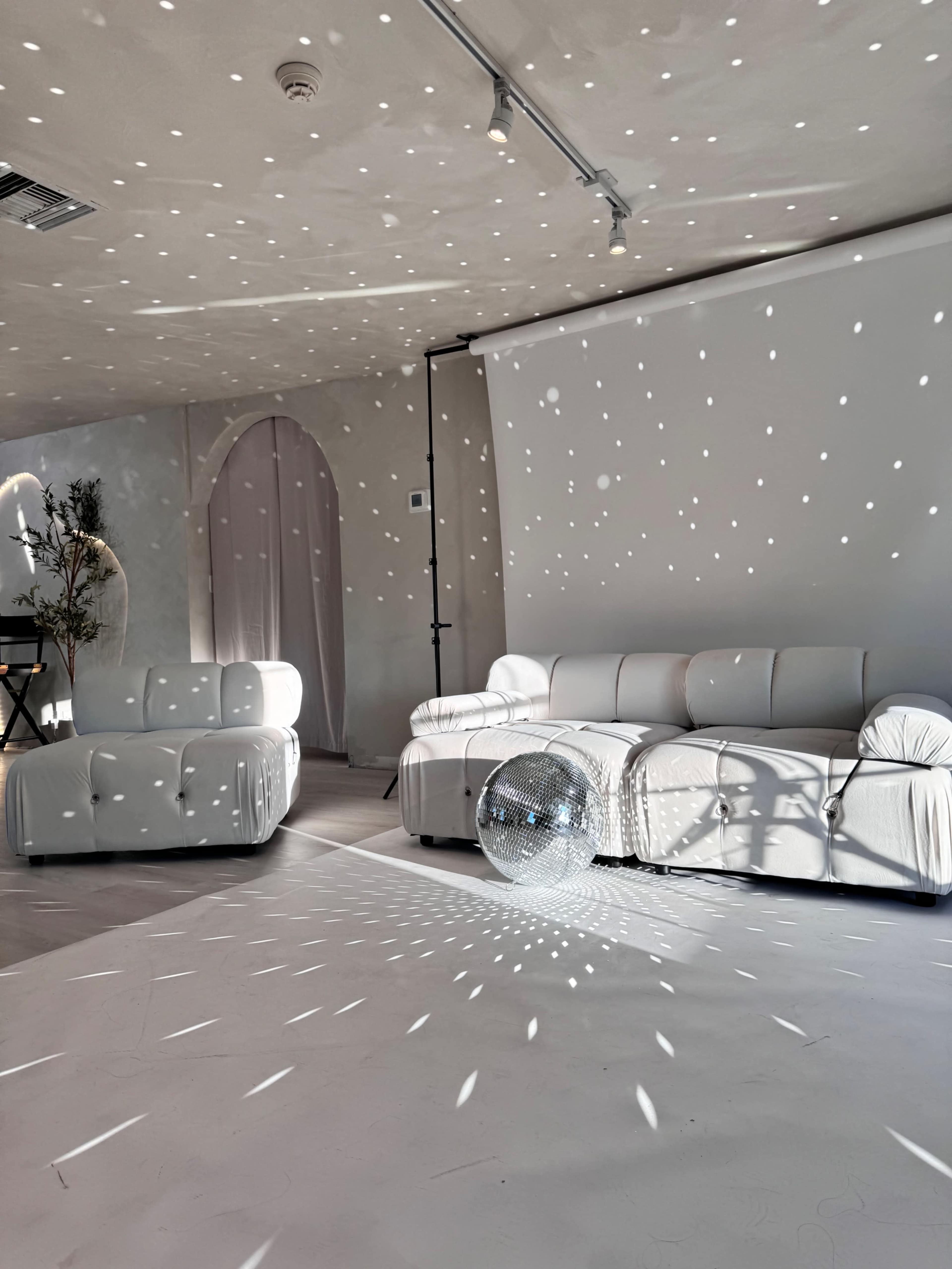 The room features white sofas and a disco ball casting light patterns on the walls and floor.