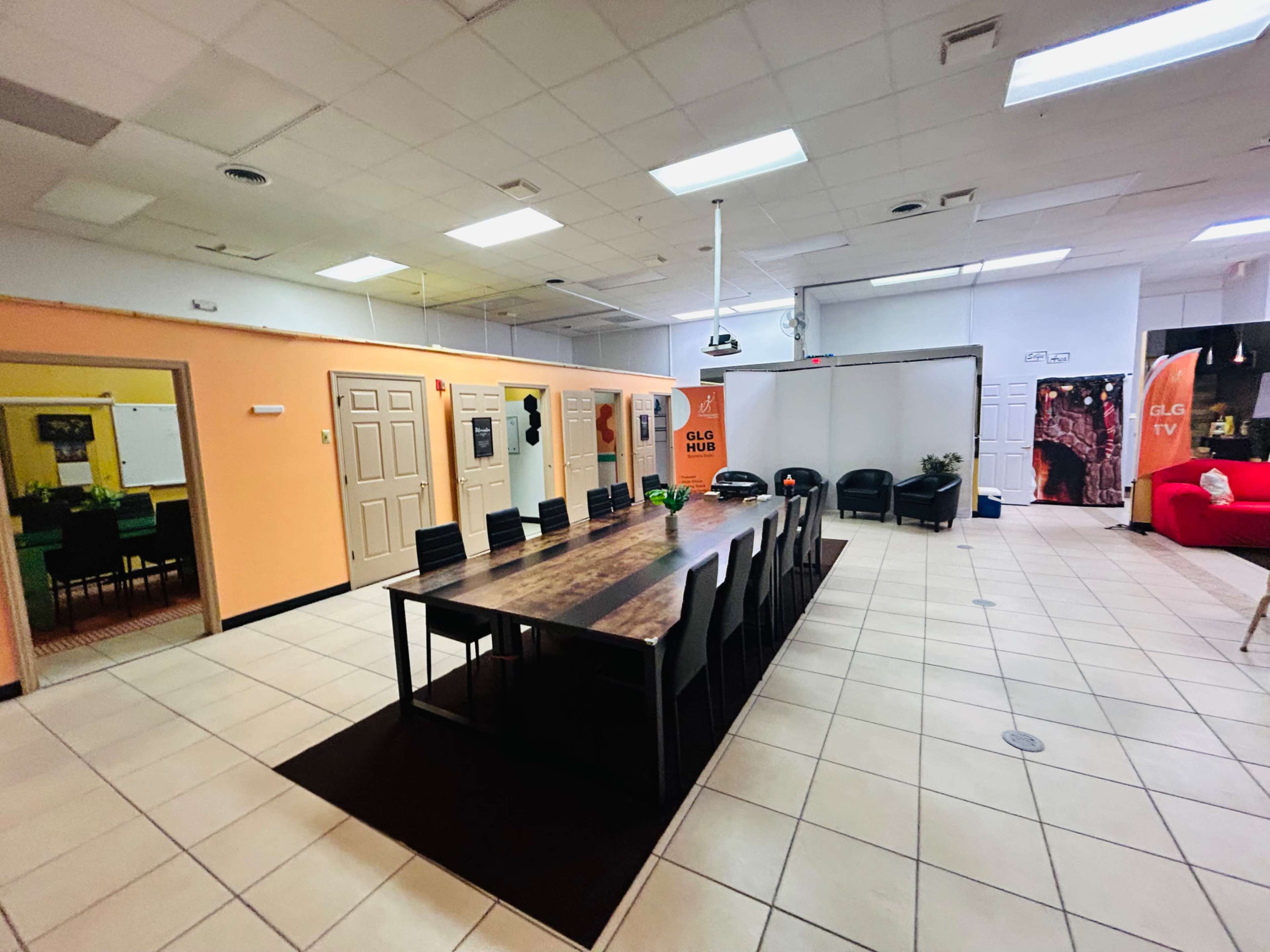 A spacious meeting room with a long wooden table and black chairs, flanked by orange and neutral-colored walls, and equipped with a projector.