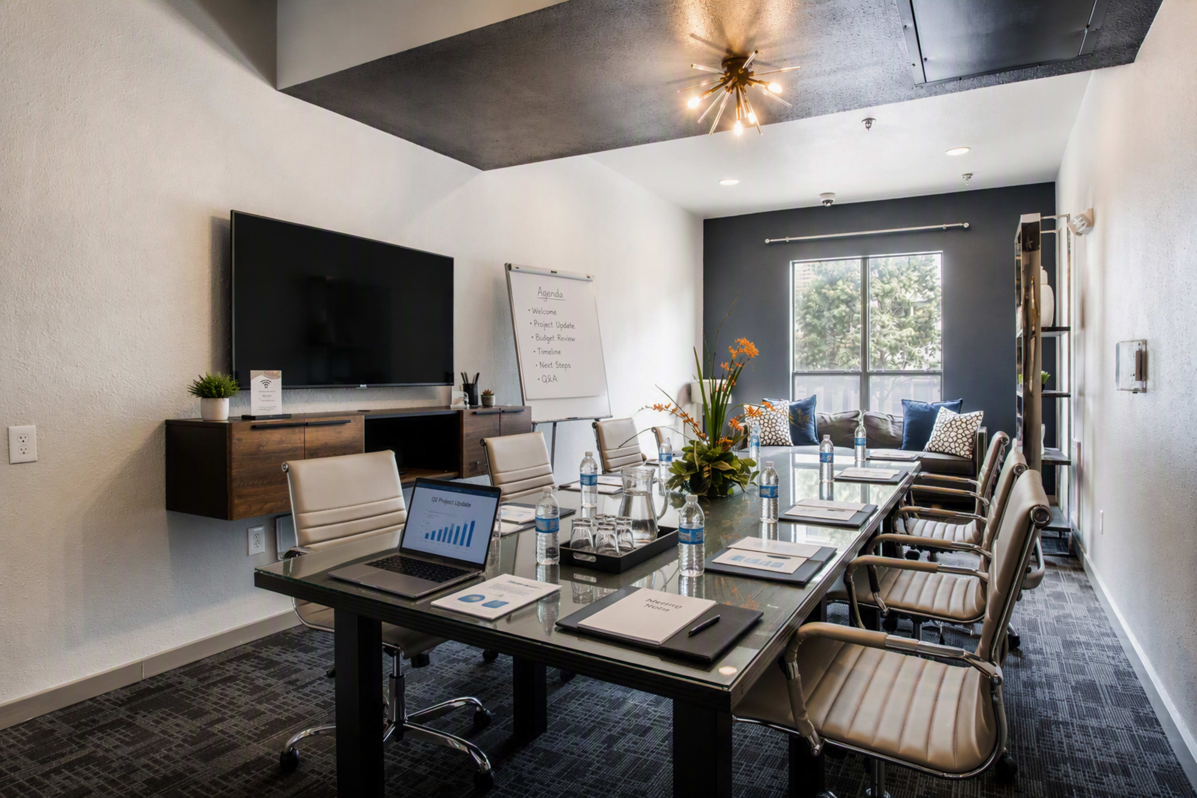 The image shows a modern conference room equipped with a large table, chairs, and a presentation screen, featuring a view of a window and a whiteboard.