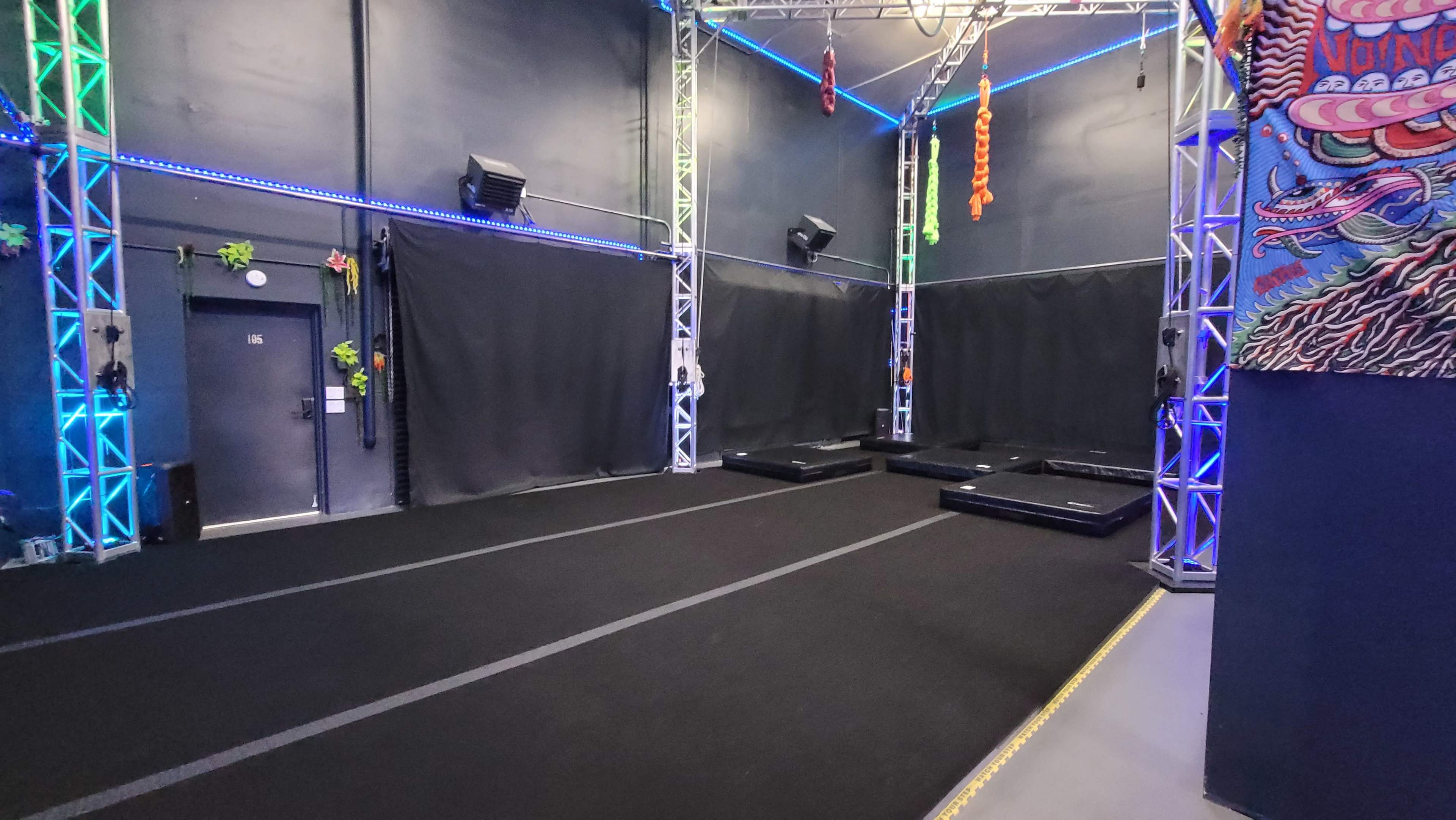 An indoor space with black carpeting and multiple wall-mounted structures featuring colorful lights and black curtains.