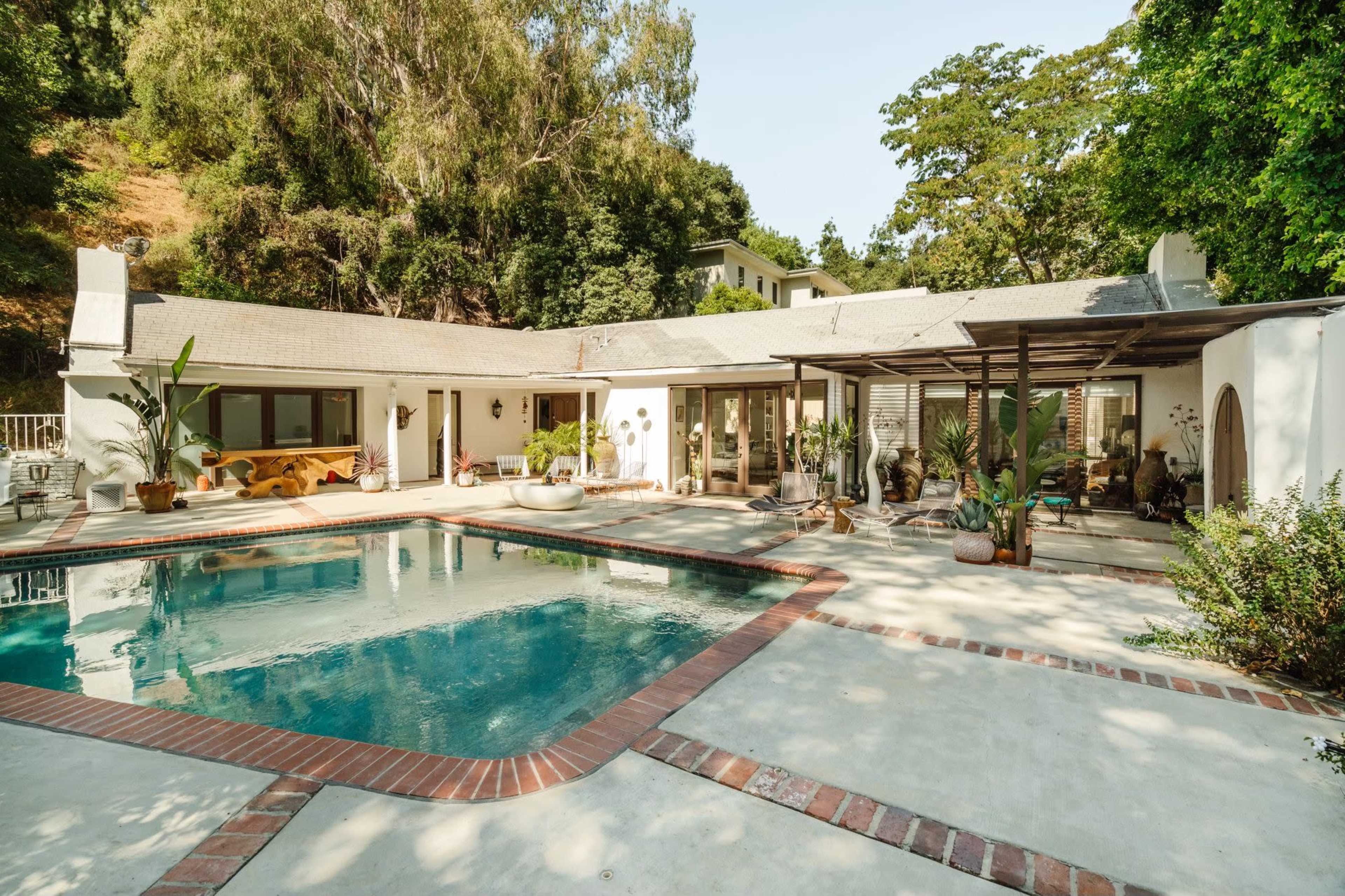 The image shows a modern home with a pool, surrounded by trees and landscaped patio areas.