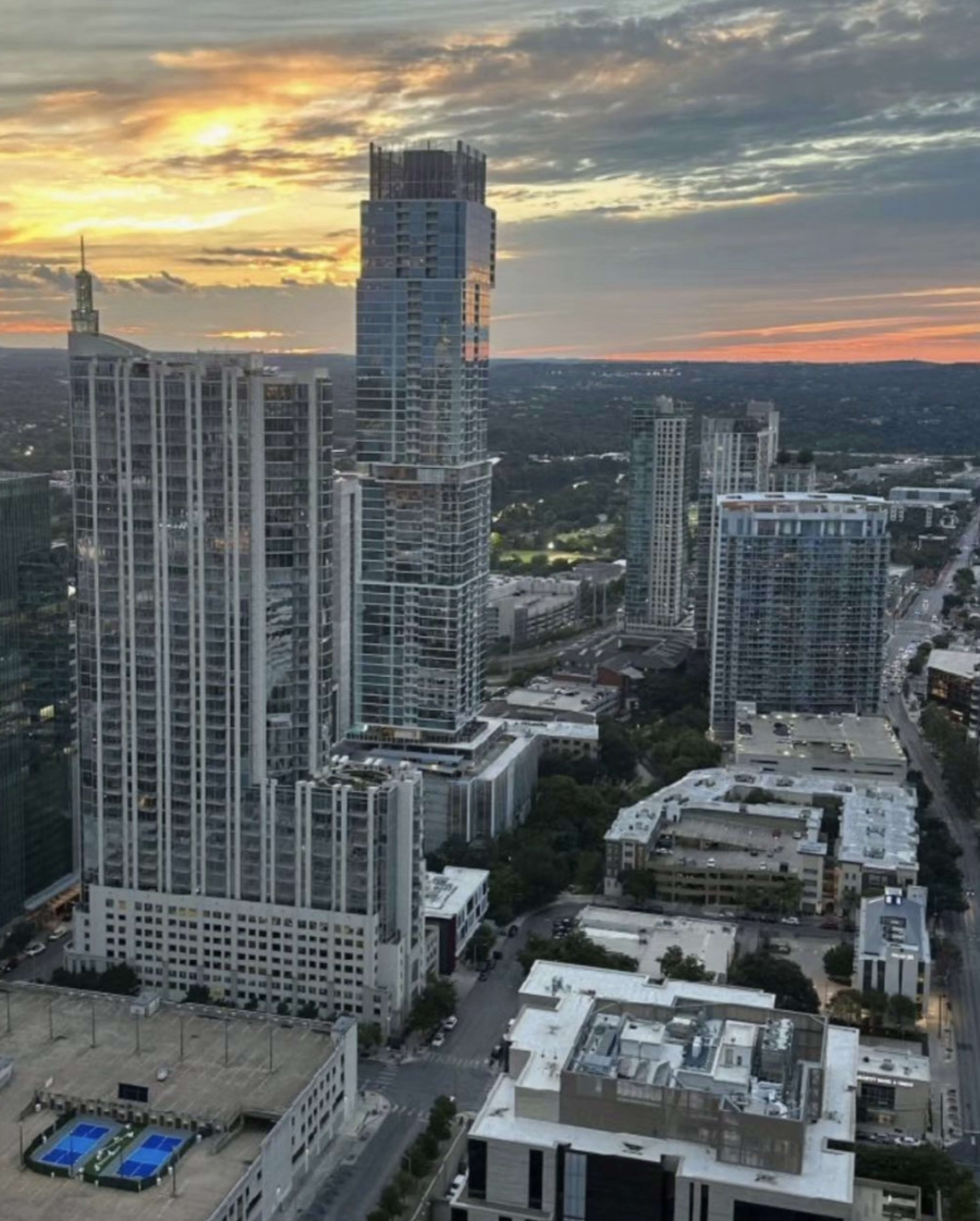 A skyline view of tall buildings at sunset, with scattered clouds in the sky and a blue pool visible in the foreground.
