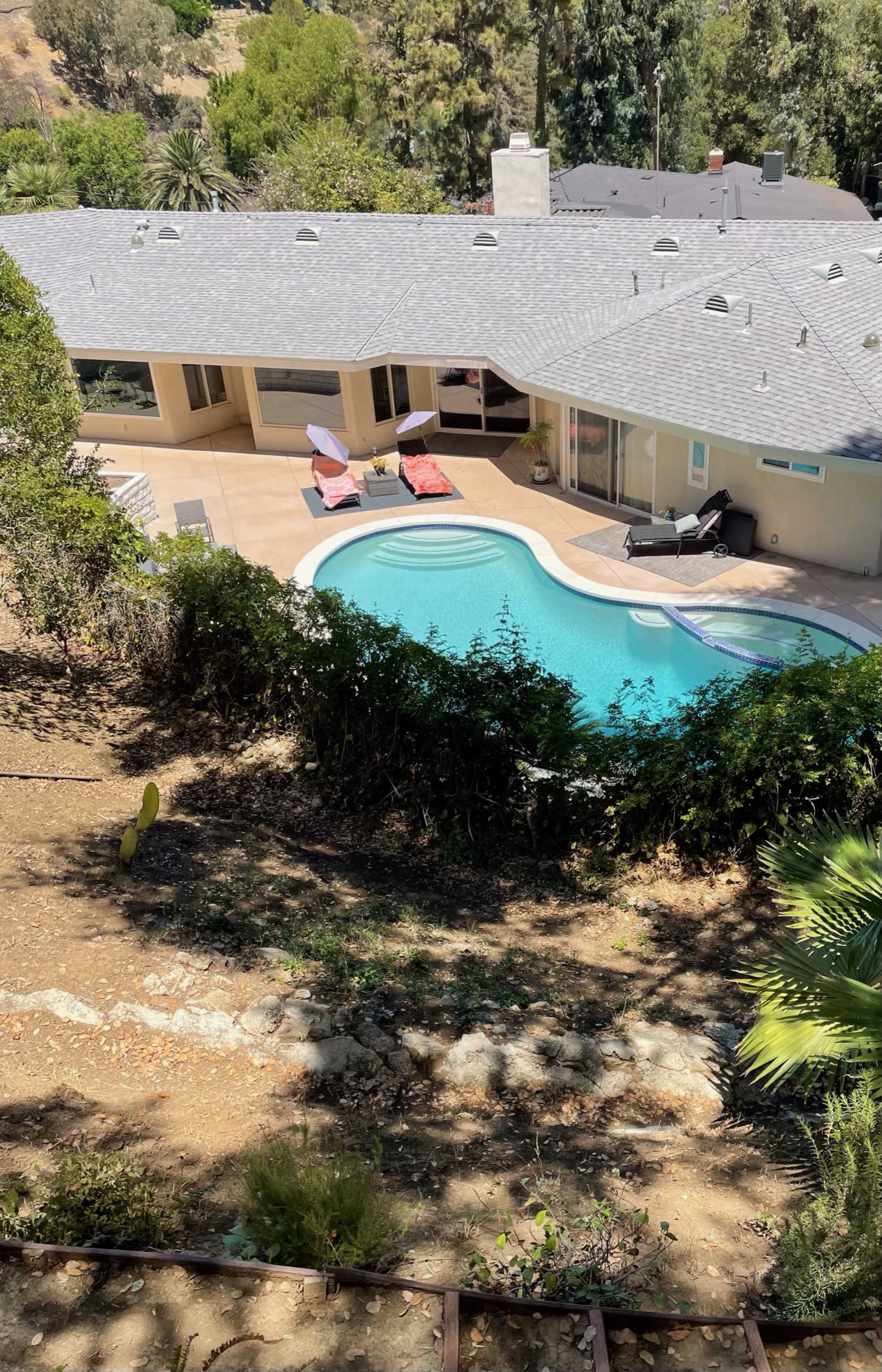 A modern house with a swimming pool surrounded by greenery is nestled in a hillside setting.