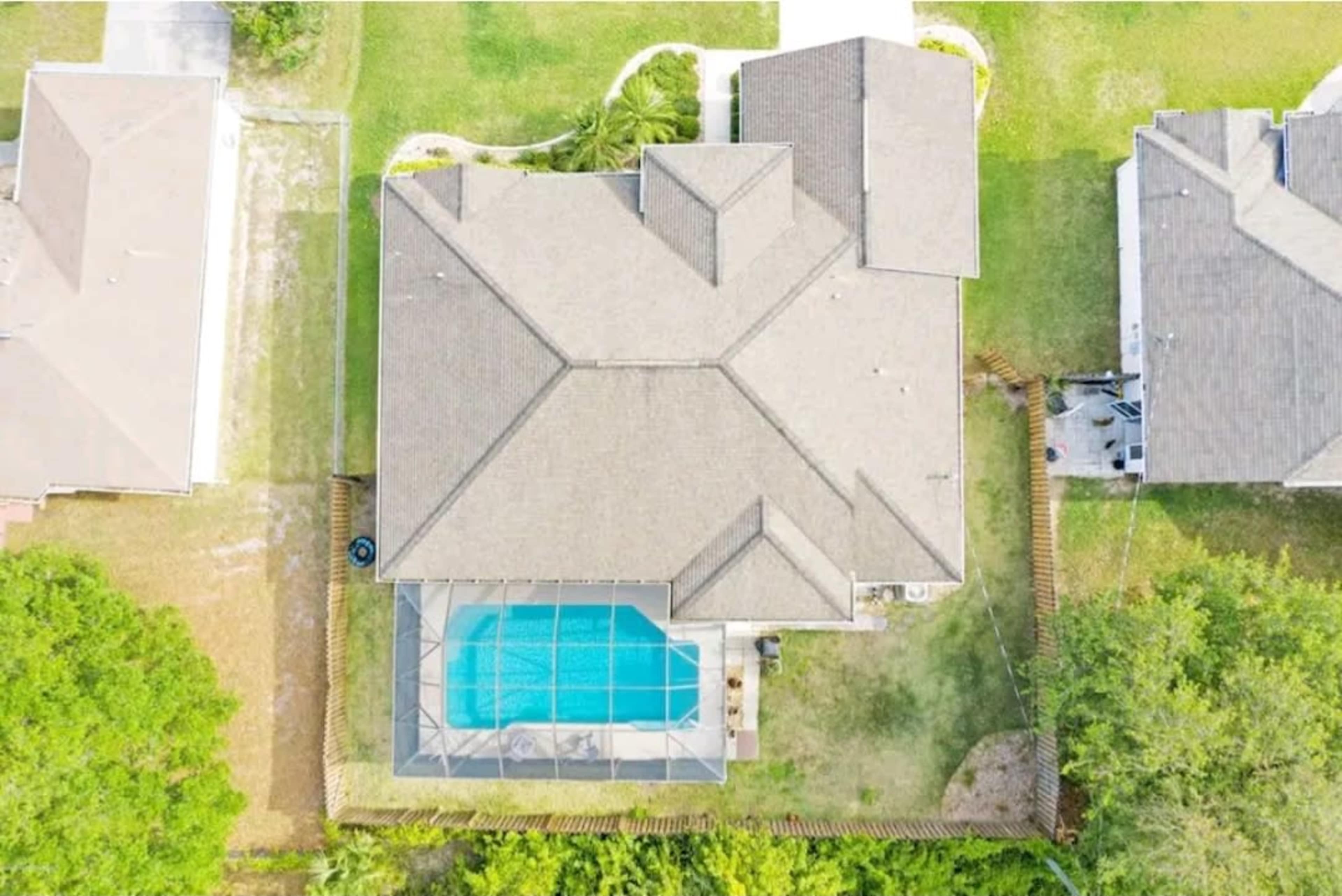 An aerial view shows a large house with a pool enclosed by a screen, surrounded by green grass and trees.