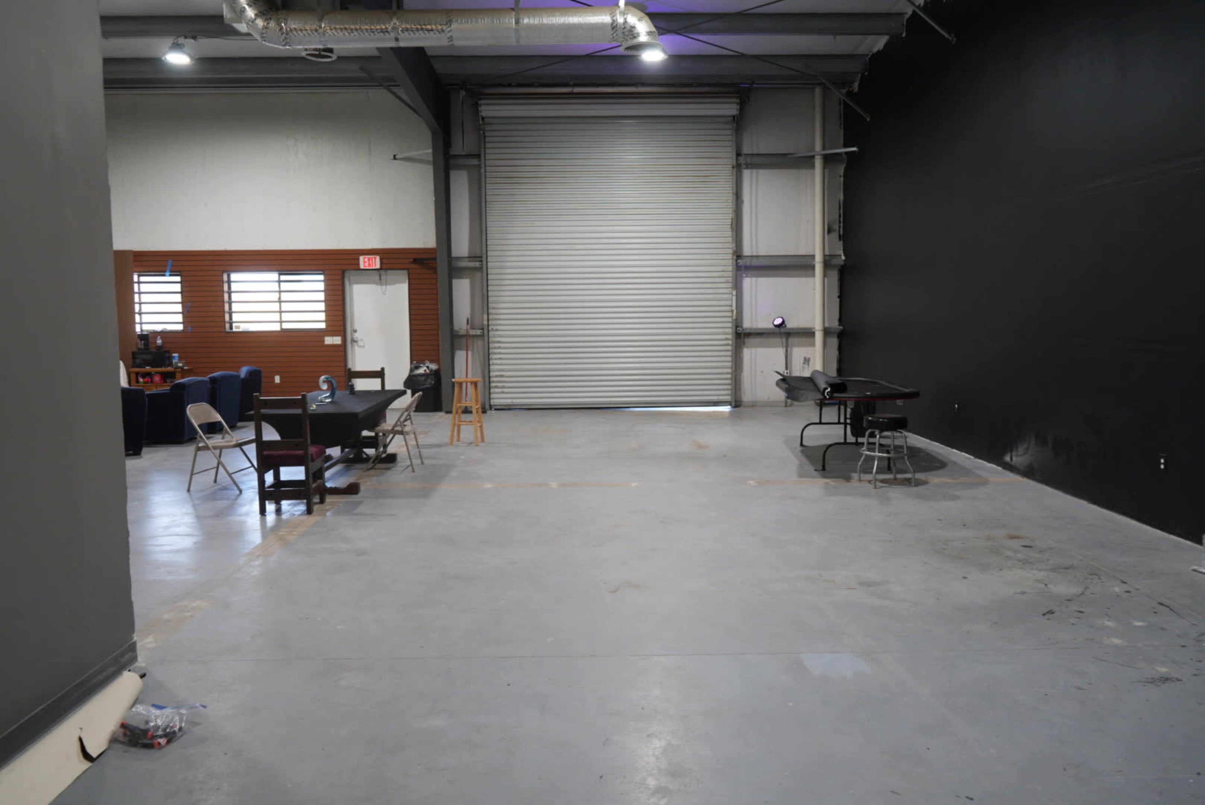 The image shows a spacious, empty industrial room with a gray concrete floor and a large roll-up door on one side.