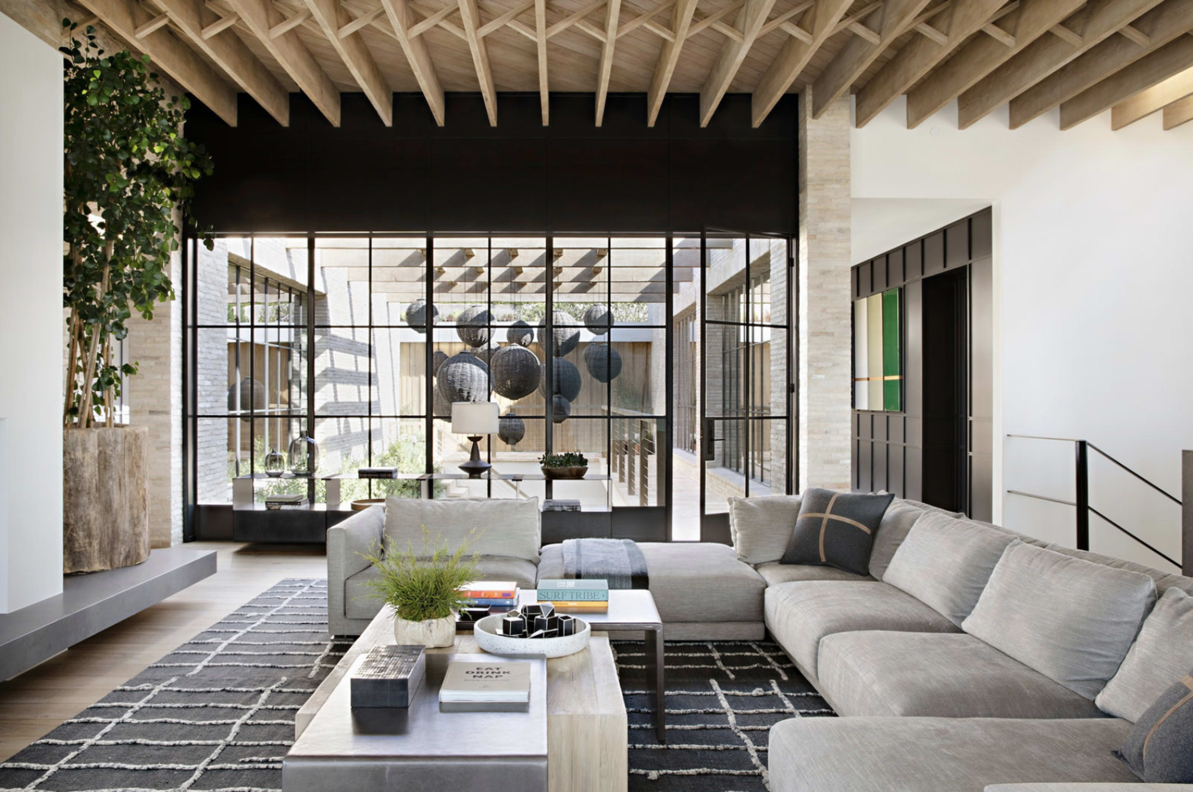 A modern living room featuring a large sectional sofa, a coffee table, and large glass windows that provide a view of an outdoor space with decorative hanging elements.