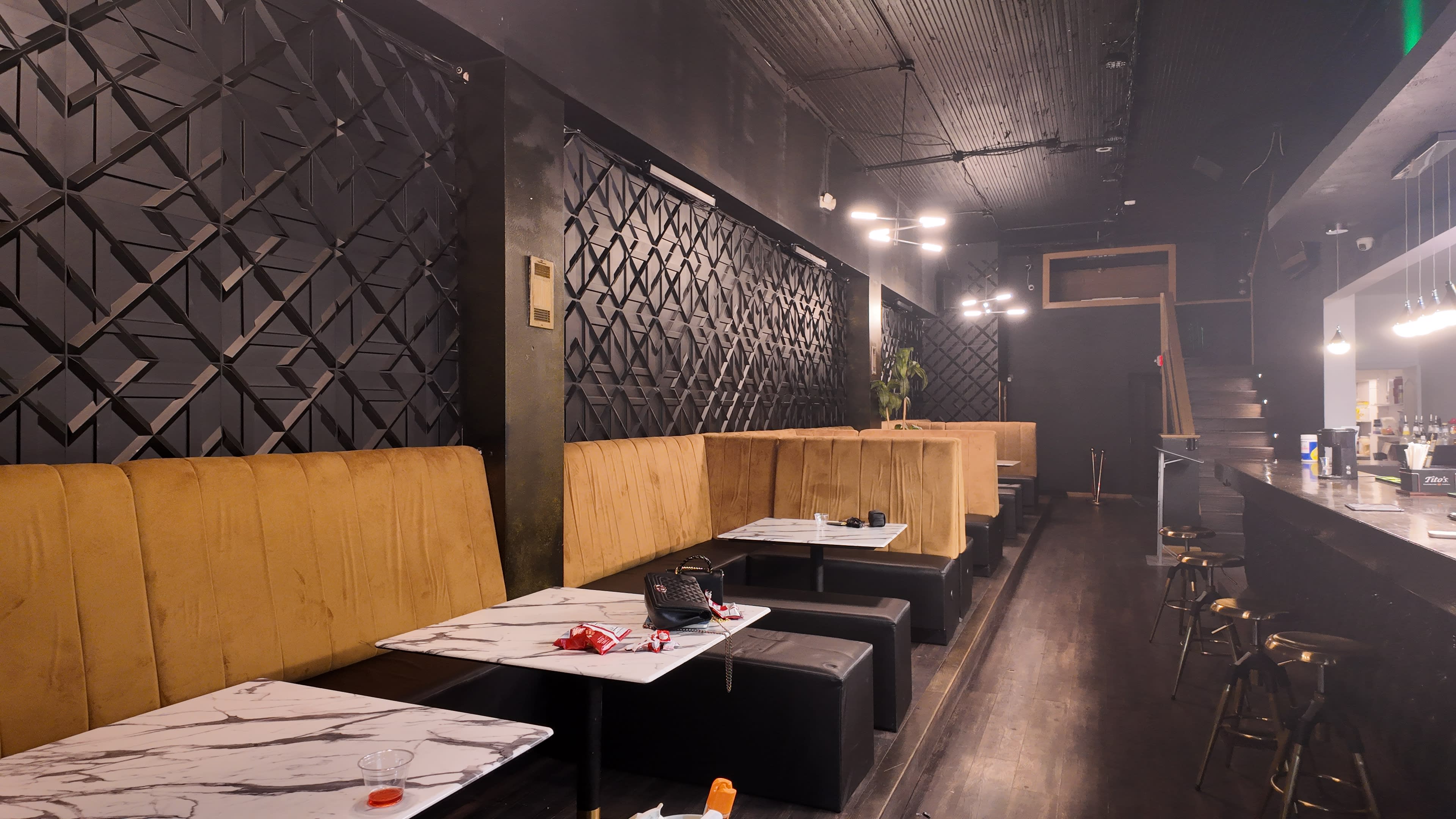 The image shows a sleek bar interior featuring plush seating booths along the walls, marble-topped tables, and a well-lit bar area at the back.