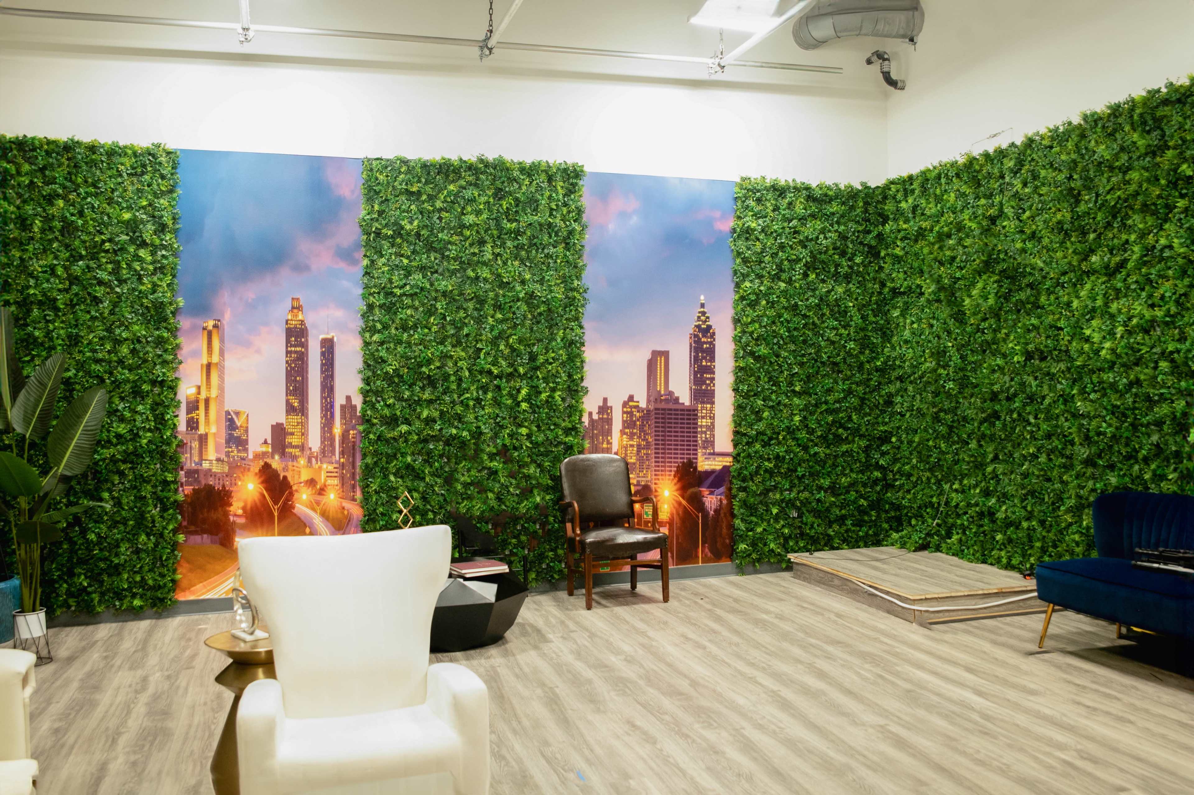 The image shows a room with green wall paneling resembling foliage, featuring two large city skyline murals, a white chair, a brown armchair, and a blue sofa.