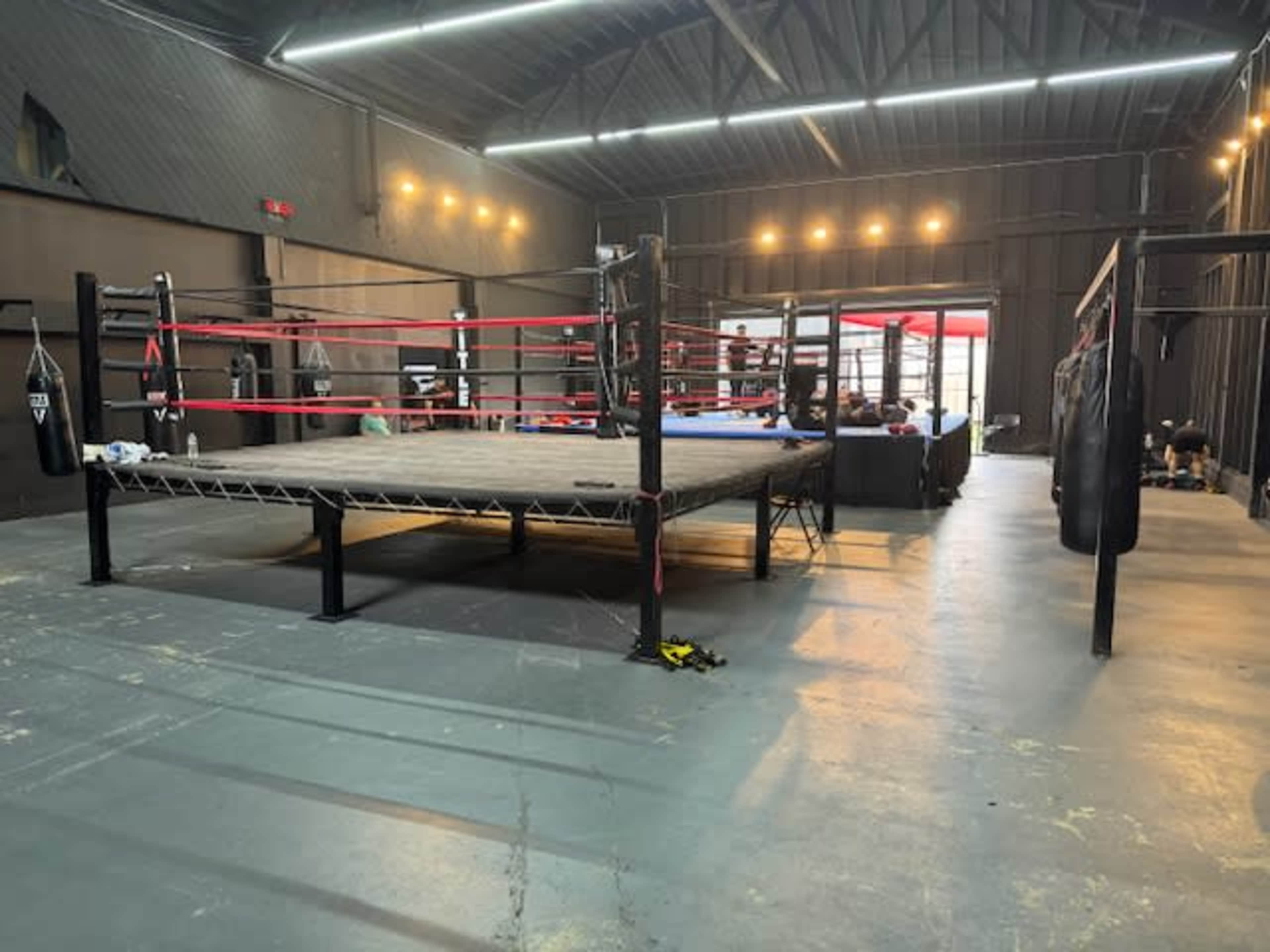 An empty boxing gym with a central ring surrounded by punching bags and training equipment.