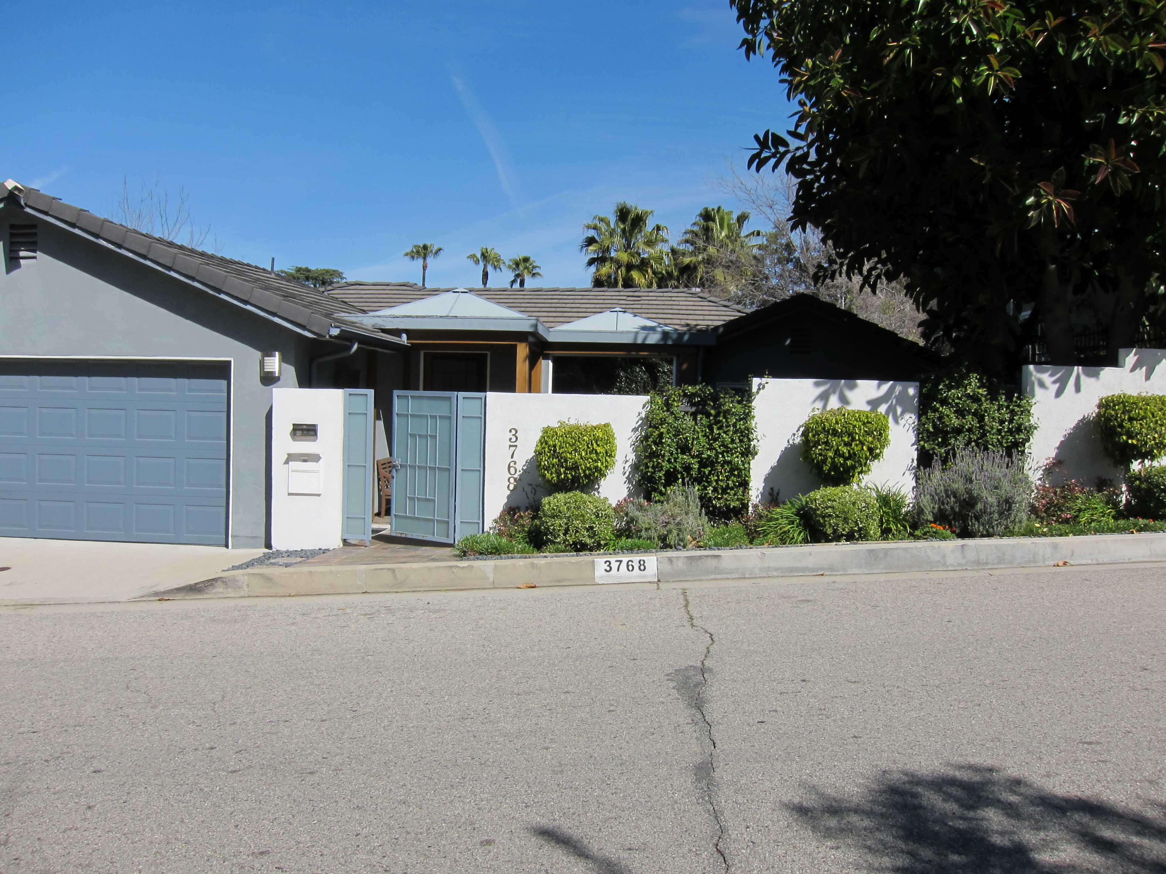 A single-story house with a gray garage door, a decorative front gate, and neatly trimmed landscaping along the sidewalk.