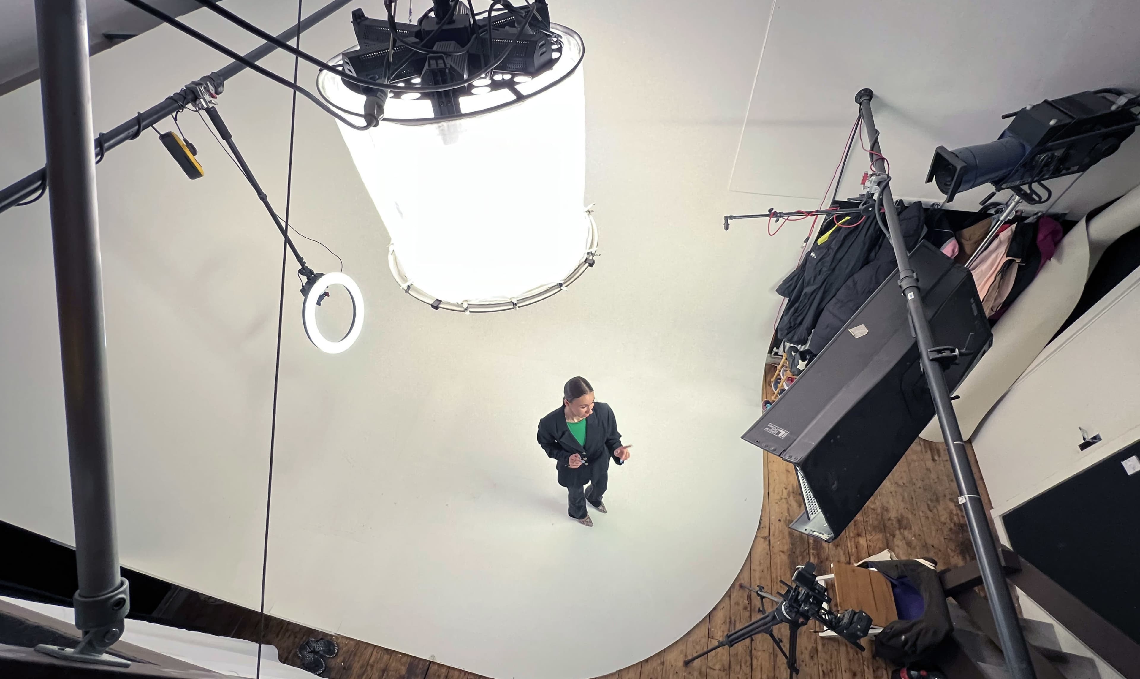 A person stands in a studio with a circular white backdrop, surrounded by studio lighting and camera equipment.