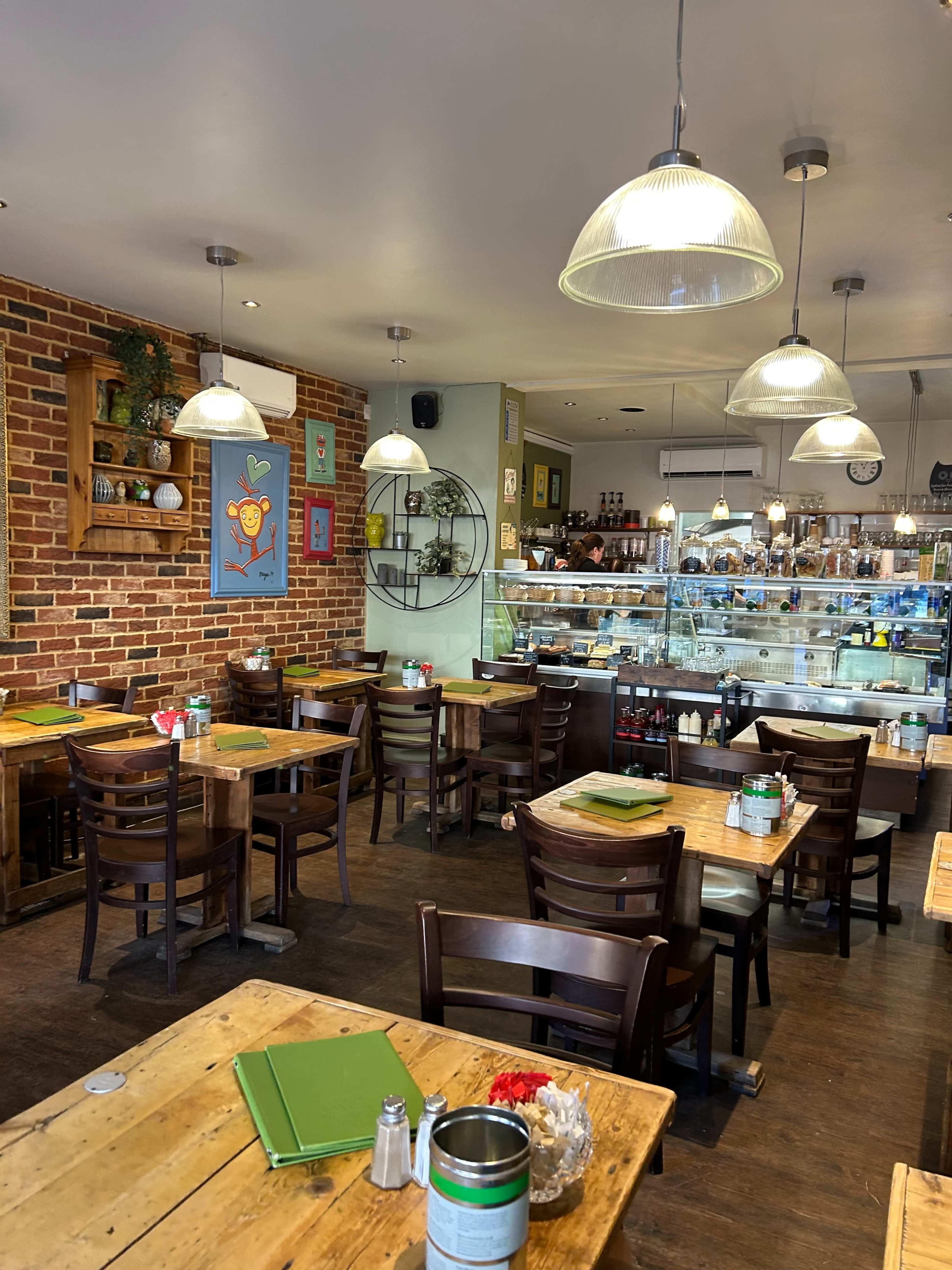 A cozy café interior with wooden tables, chairs, and a glass display case, all surrounded by exposed brick walls and pendant lighting.