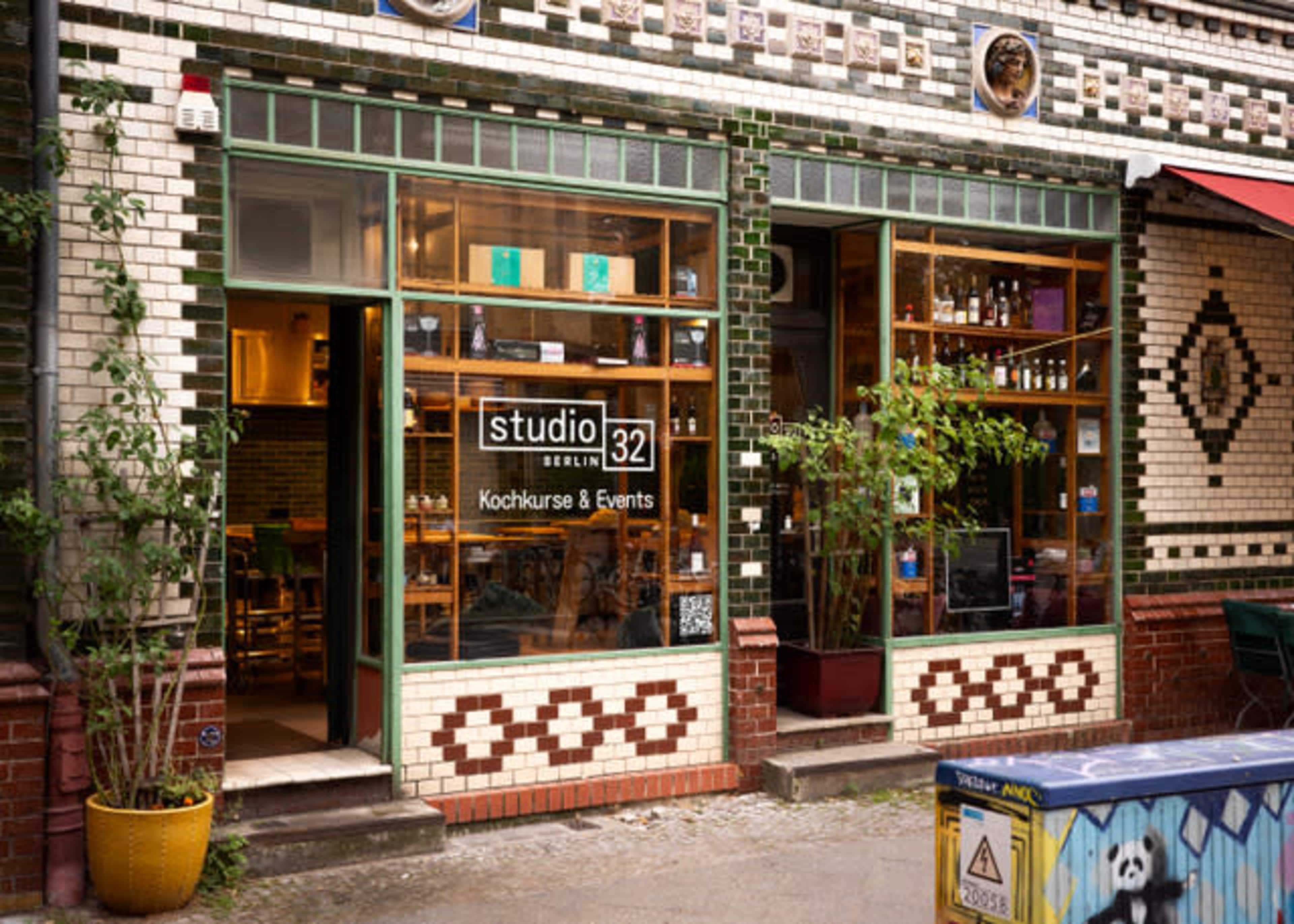 The image shows the exterior of a restaurant named "studio 32," featuring tiled walls, large windows with greenery, and outdoor seating.
