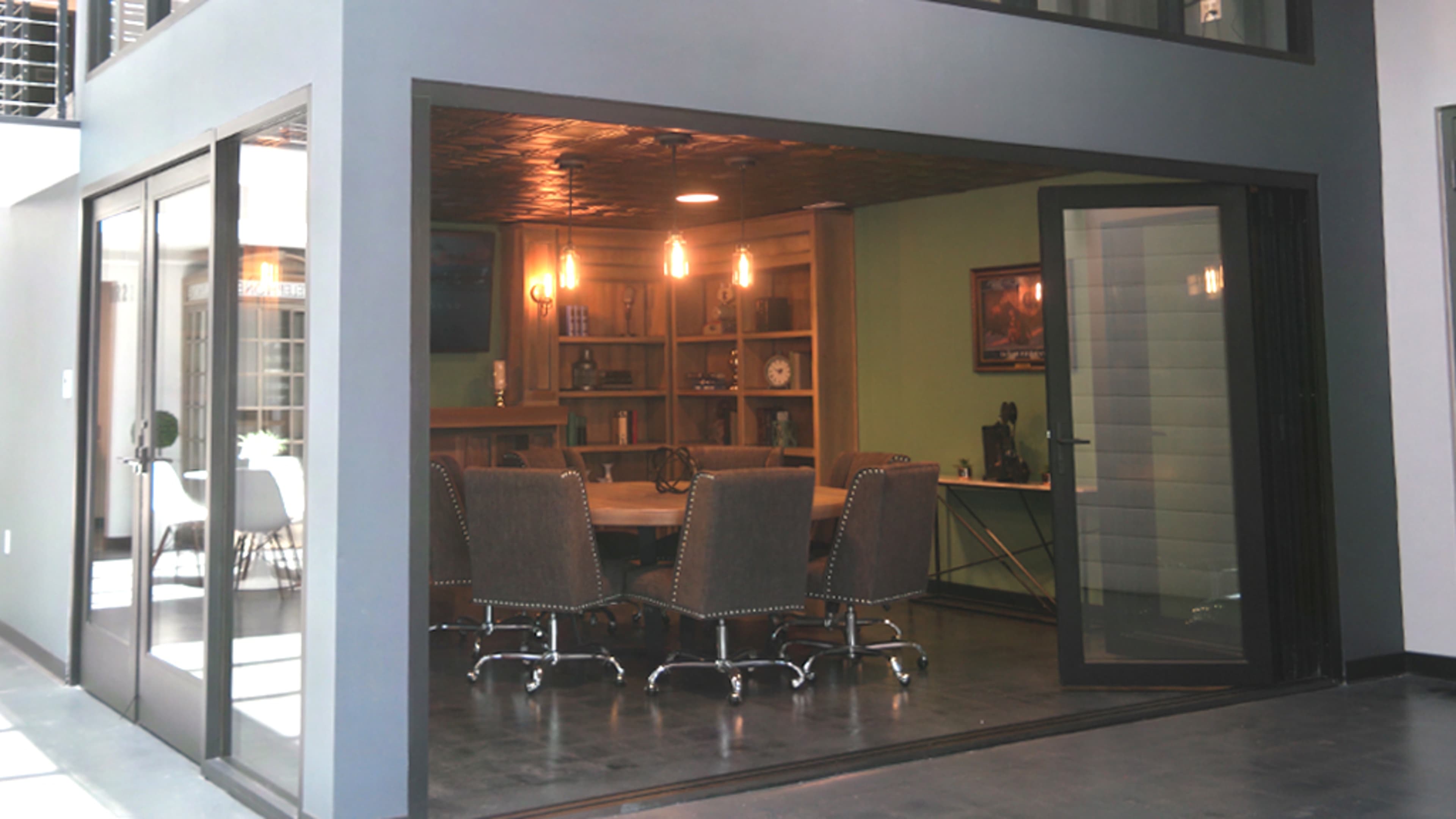 A modern conference room featuring a large wooden table surrounded by upholstered chairs and a bookshelf against the wall.