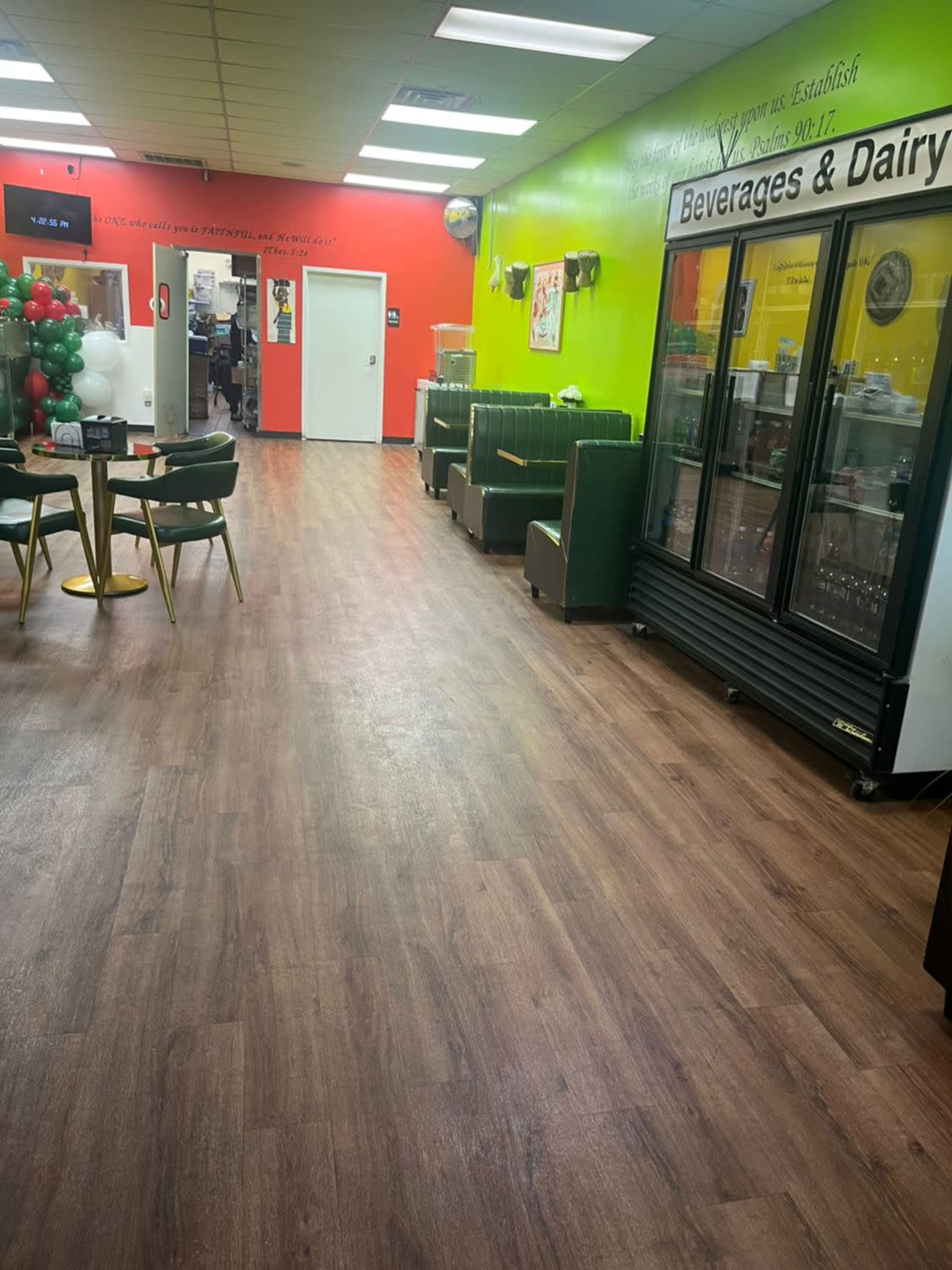 The image shows an interior space with a wooden floor, green and bright-colored walls, and a beverage refrigerator in the background.