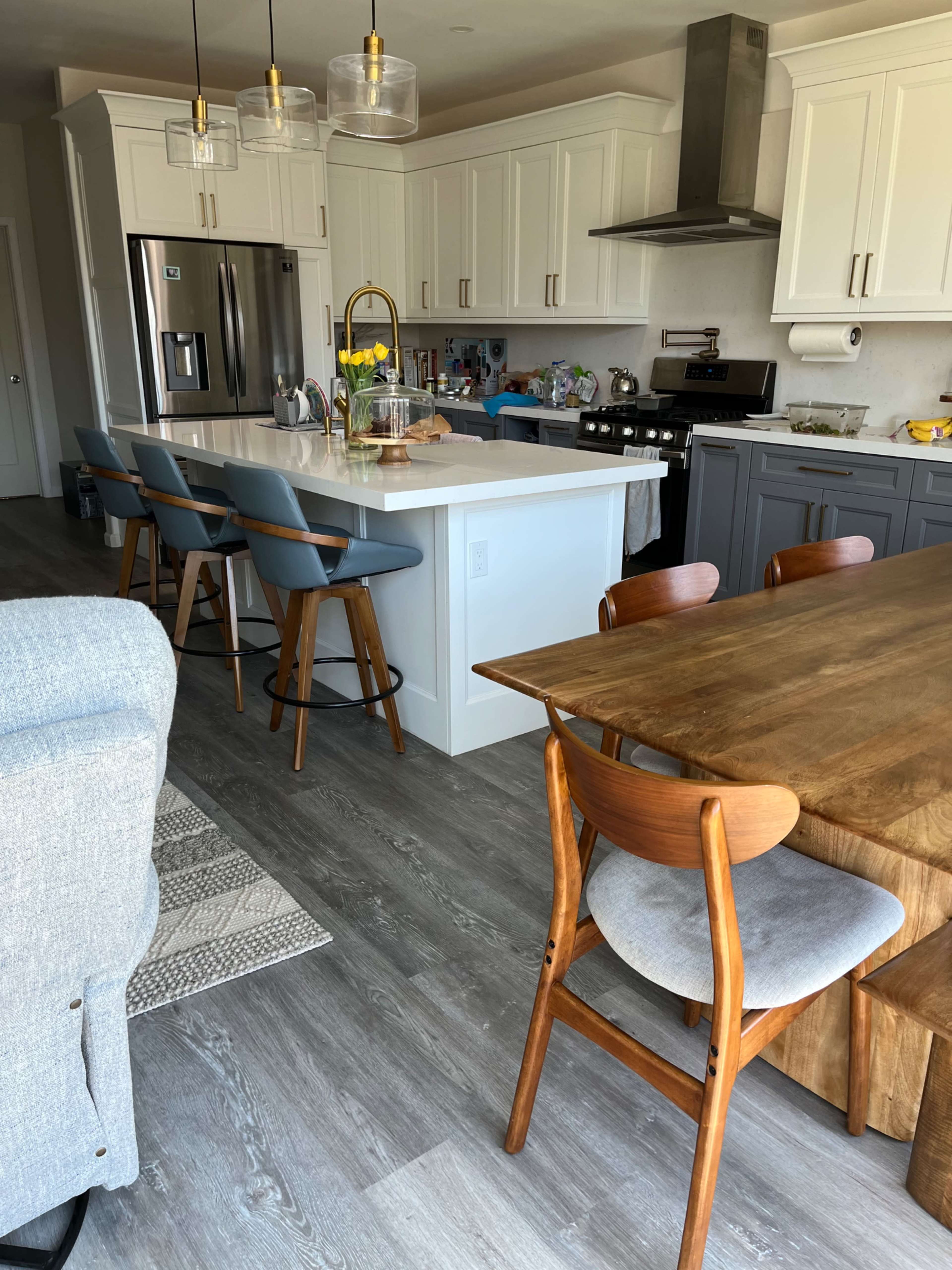 A modern kitchen featuring an island with stools, stainless steel appliances, and a wooden dining table.