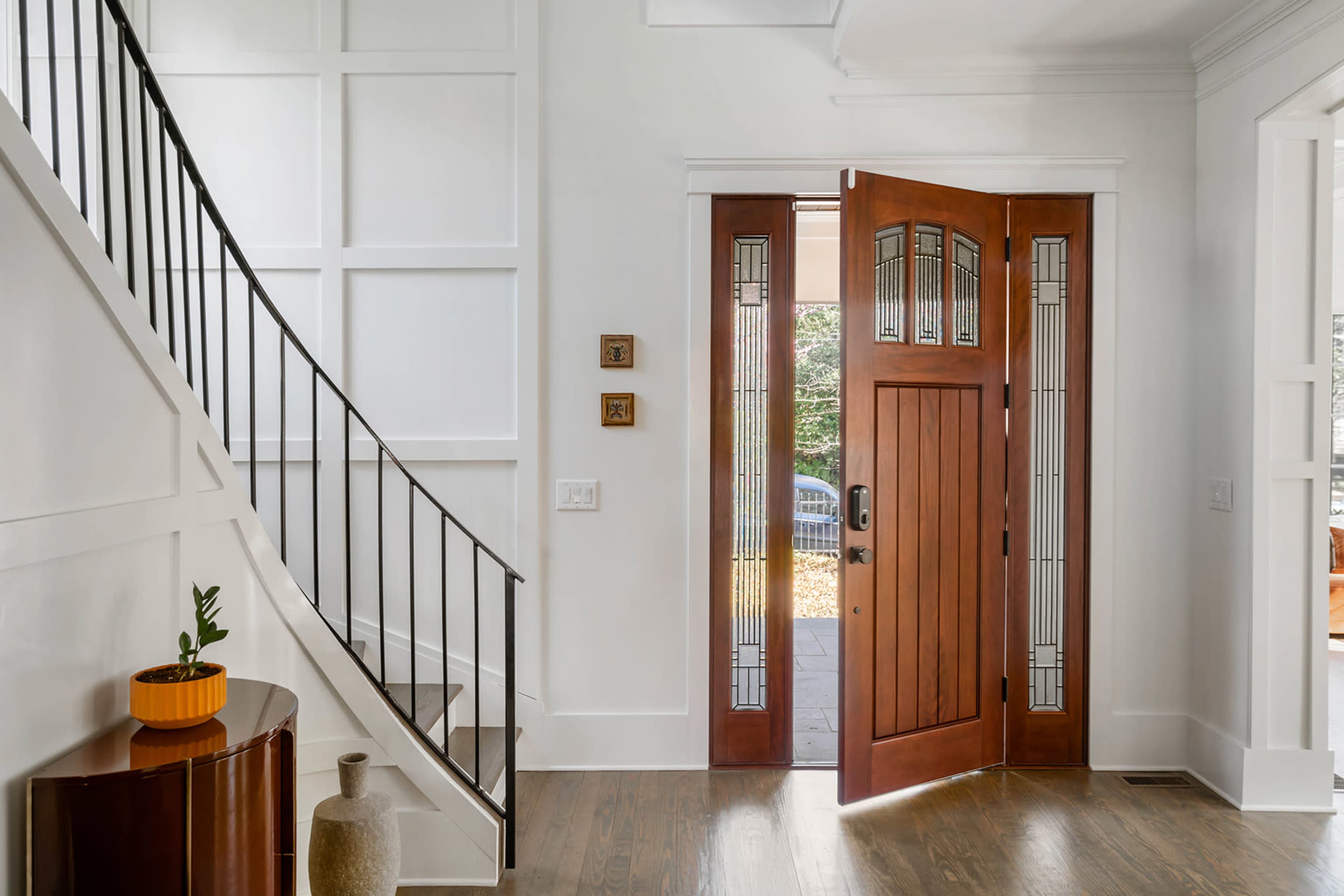 A modern entrance hall with a wooden front door open to a staircase and various decorative elements on the walls.