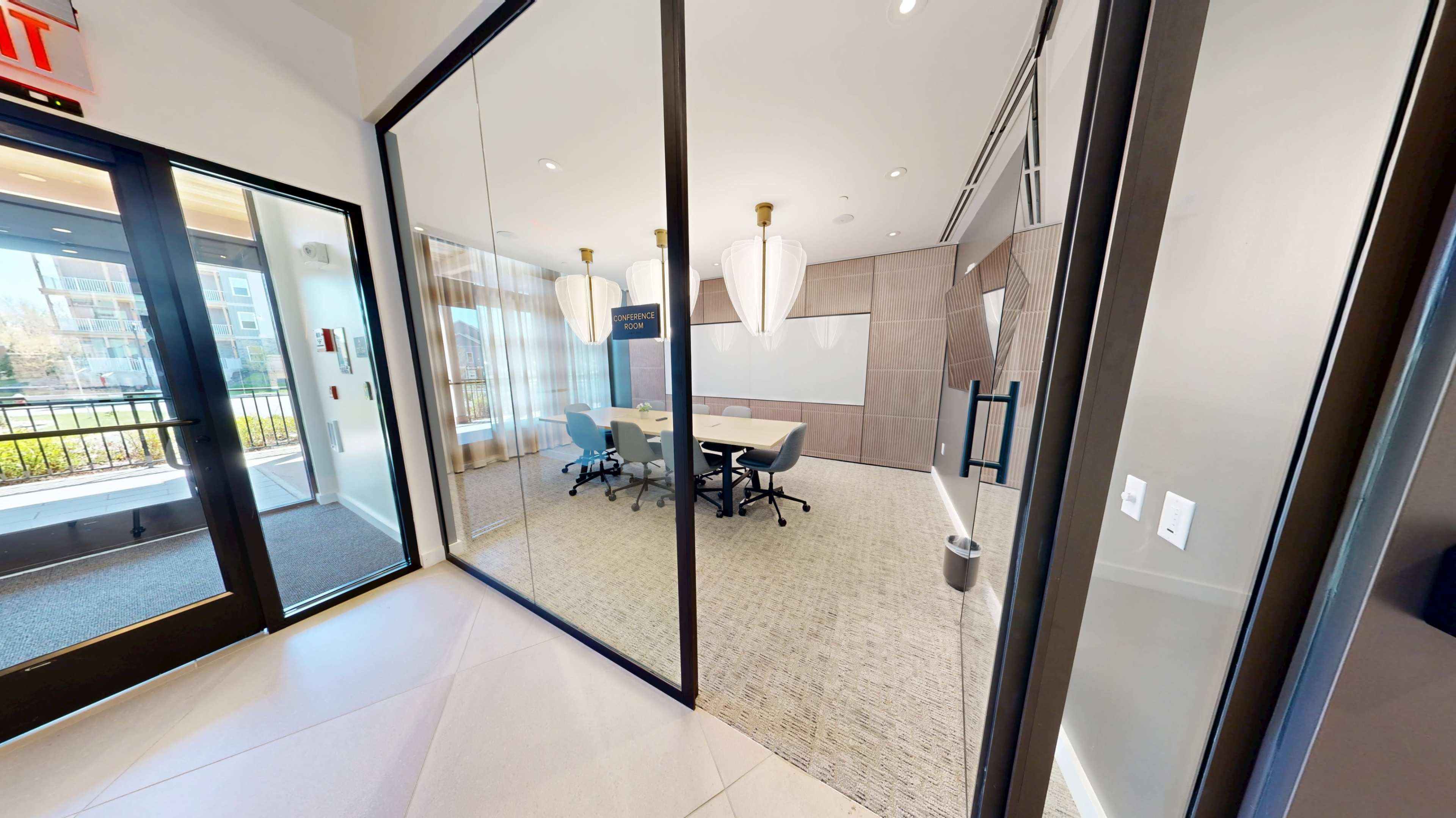The image shows a modern conference room with a large table and chairs, viewed through glass doors in an office setting.