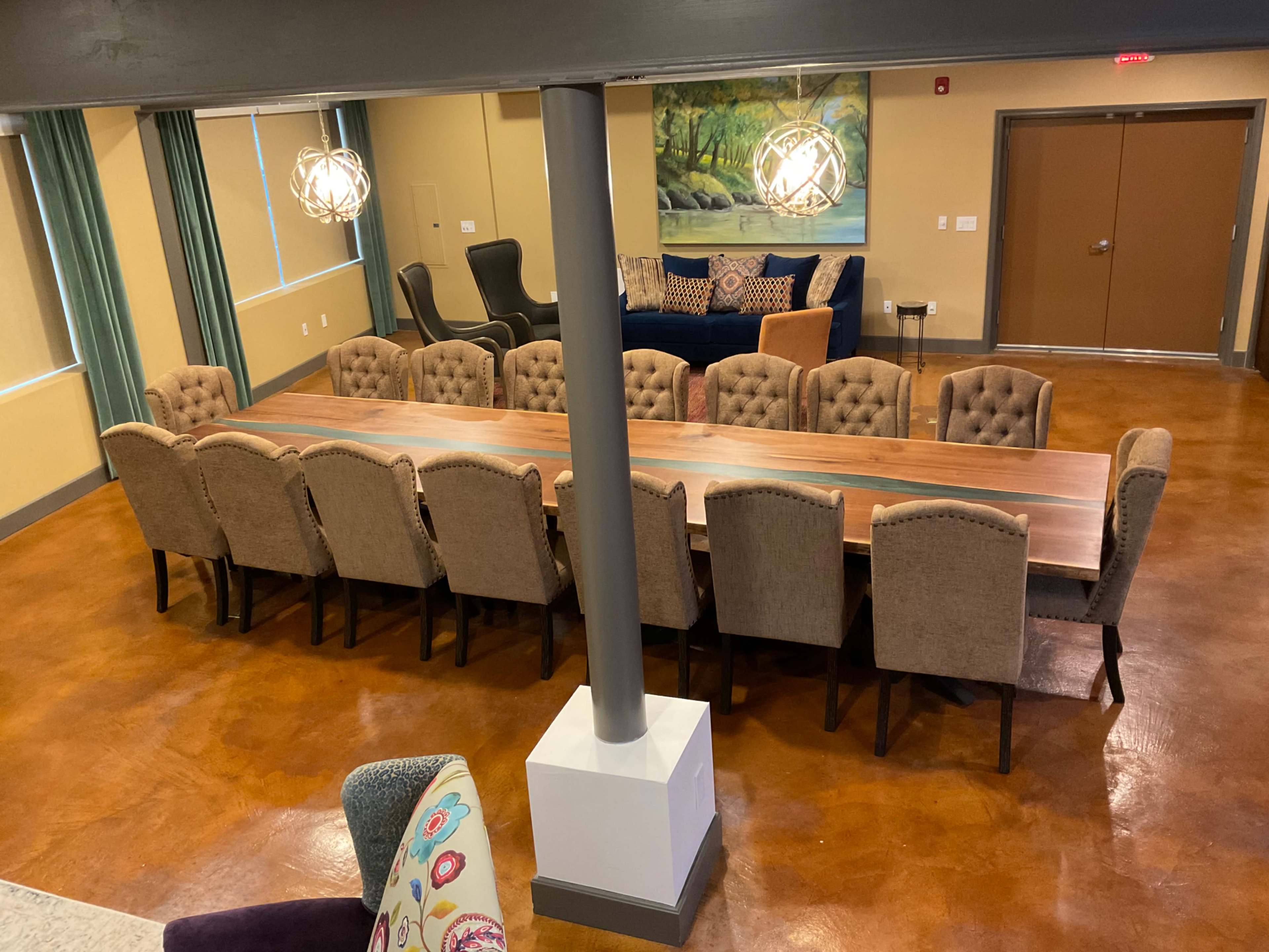A large meeting room featuring a long wooden table surrounded by upholstered chairs, with a comfortable seating area in the background.