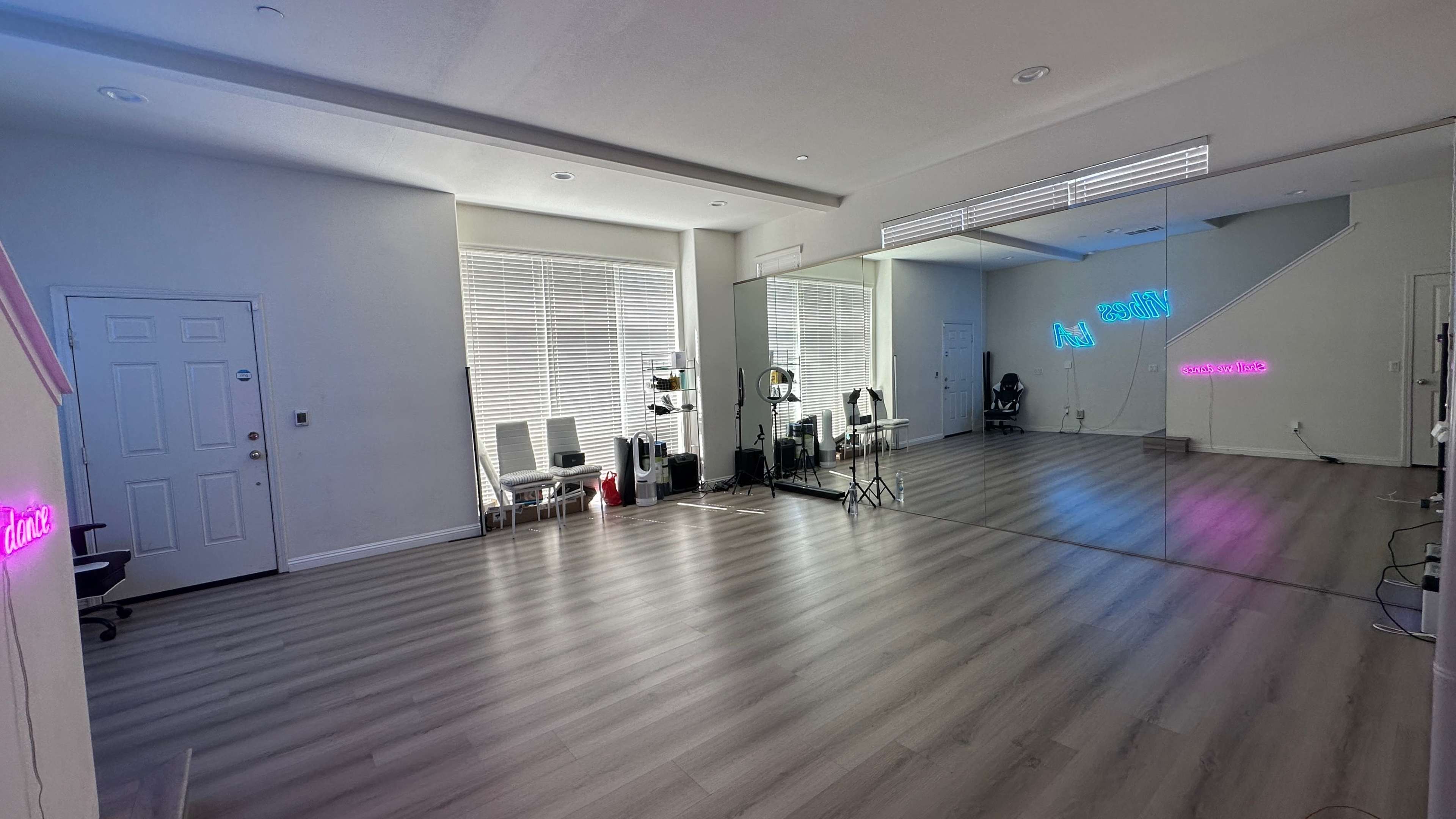 A spacious, well-lit studio with large windows, a mirrored wall, and several chairs arranged along one side.