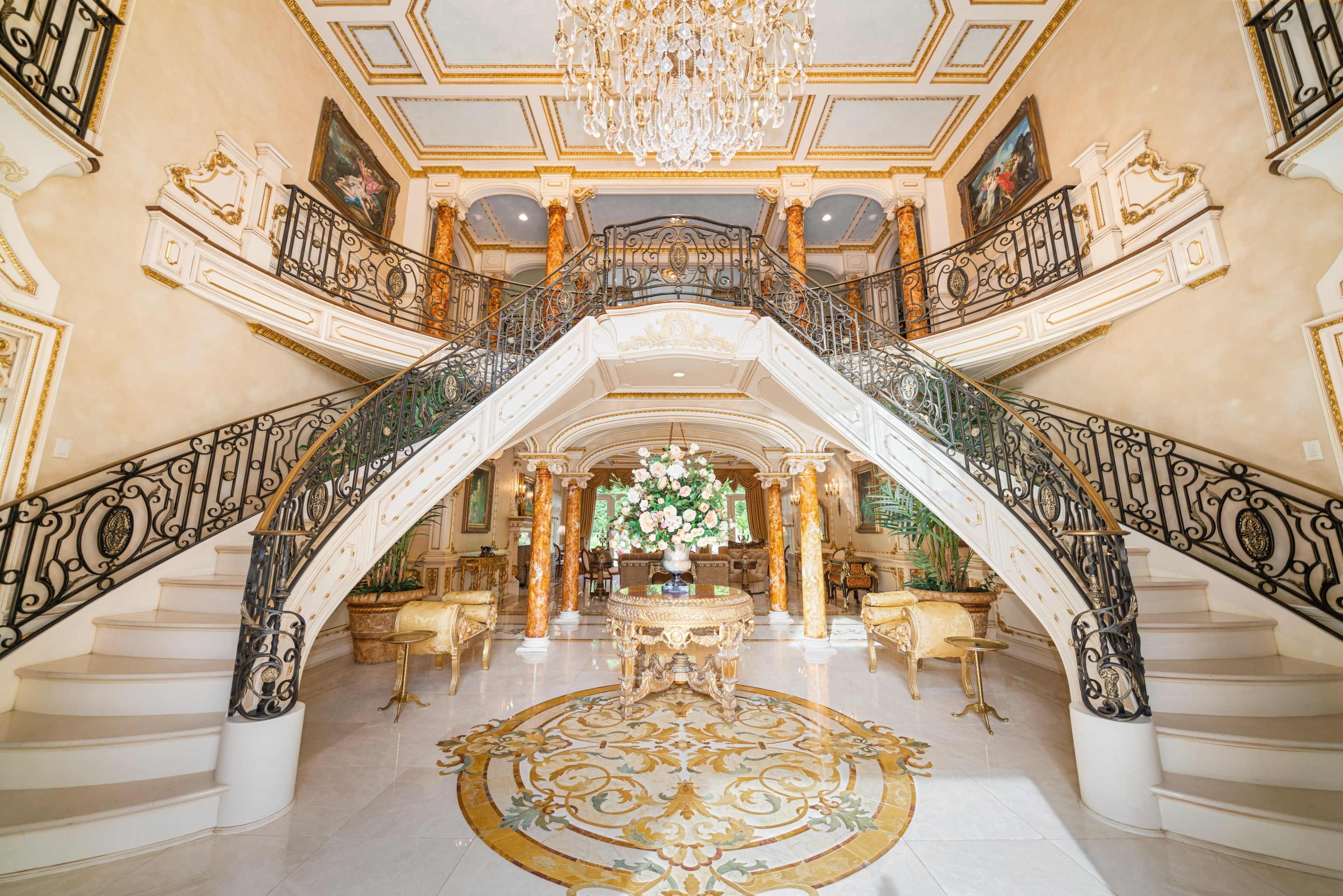 A grand entryway with a double staircase, an elaborate chandelier, and floral arrangements at the center.