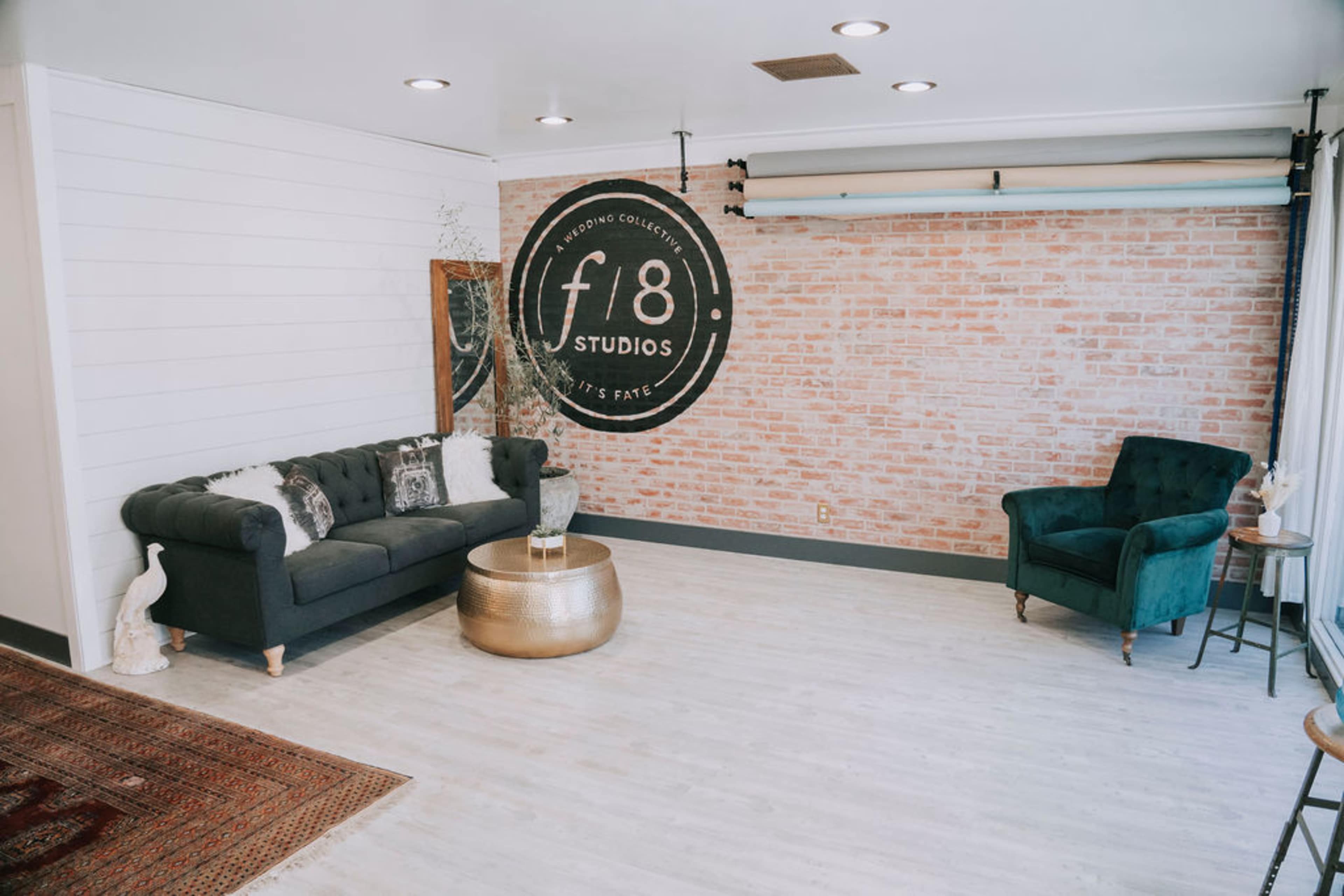 A modern studio space with a gray sofa, a green chair, and a brick accent wall featuring the logo of "f8 Studios."