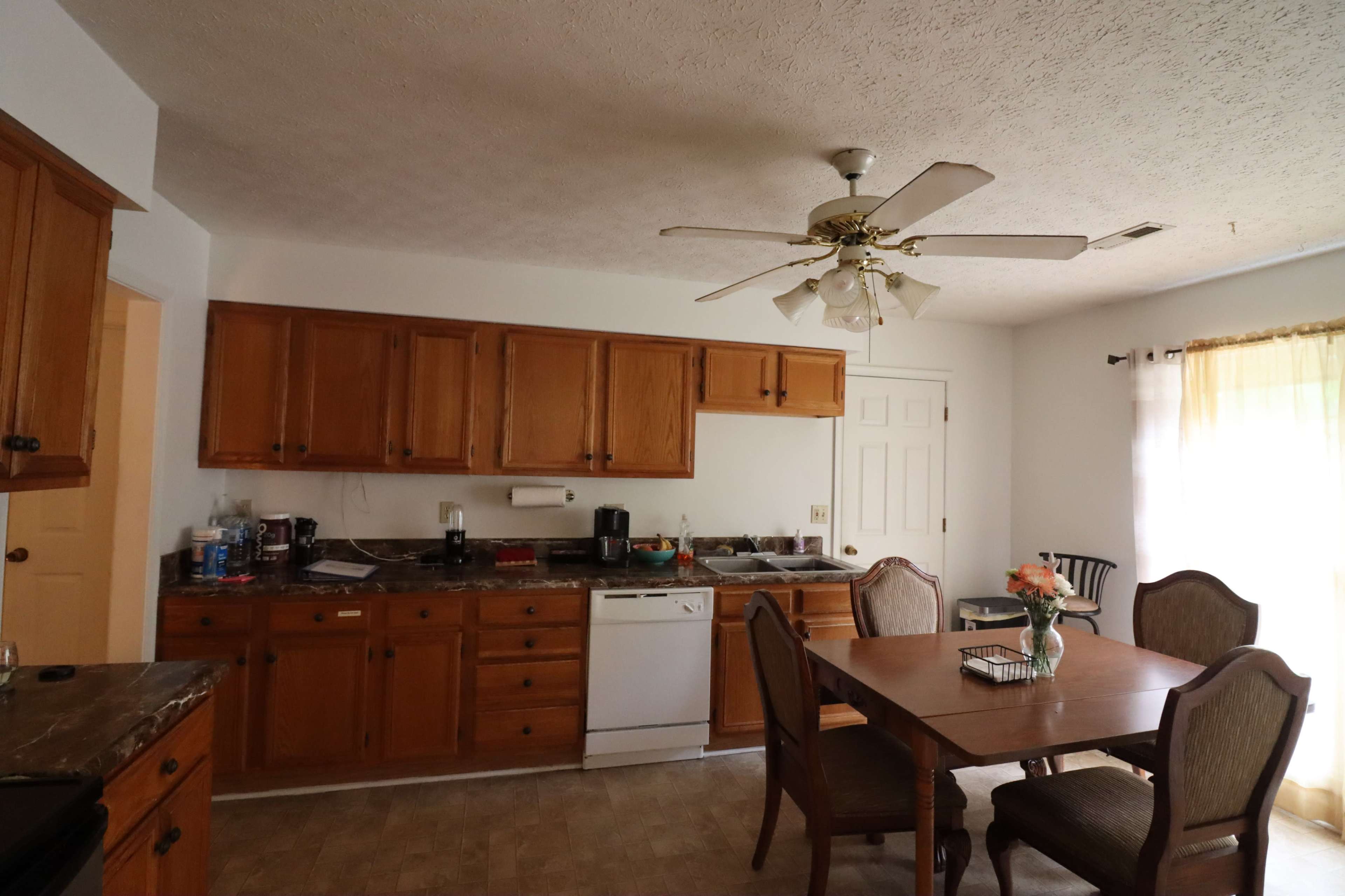 A kitchen features wooden cabinets, a dishwasher, and a dining table with chairs in a well-lit space.