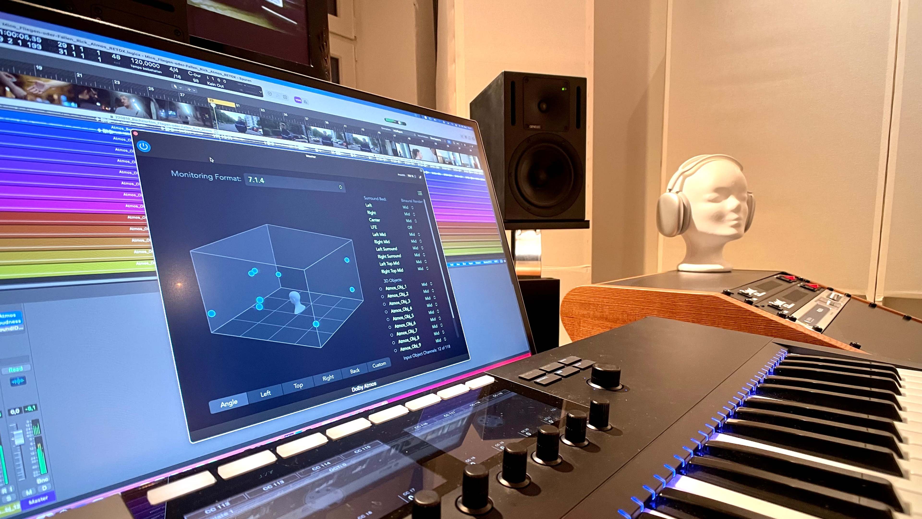 A music production workspace featuring a computer screen displaying audio monitoring software, a MIDI keyboard, and a mannequin head with headphones positioned nearby.