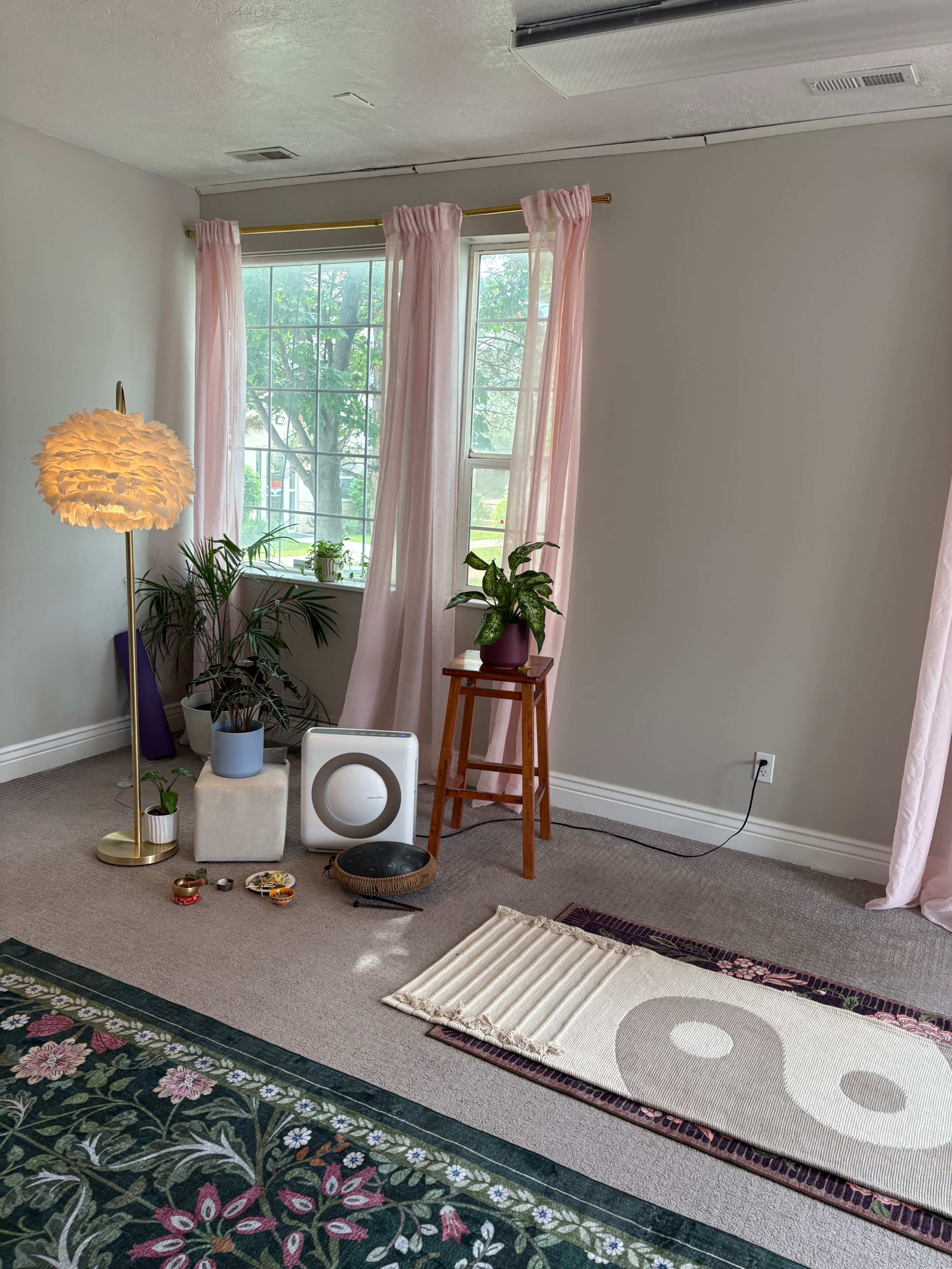 The image shows a softly lit room with pink curtains, a floor lamp, a small table with a plant, and a decorative rug featuring a yin-yang design.