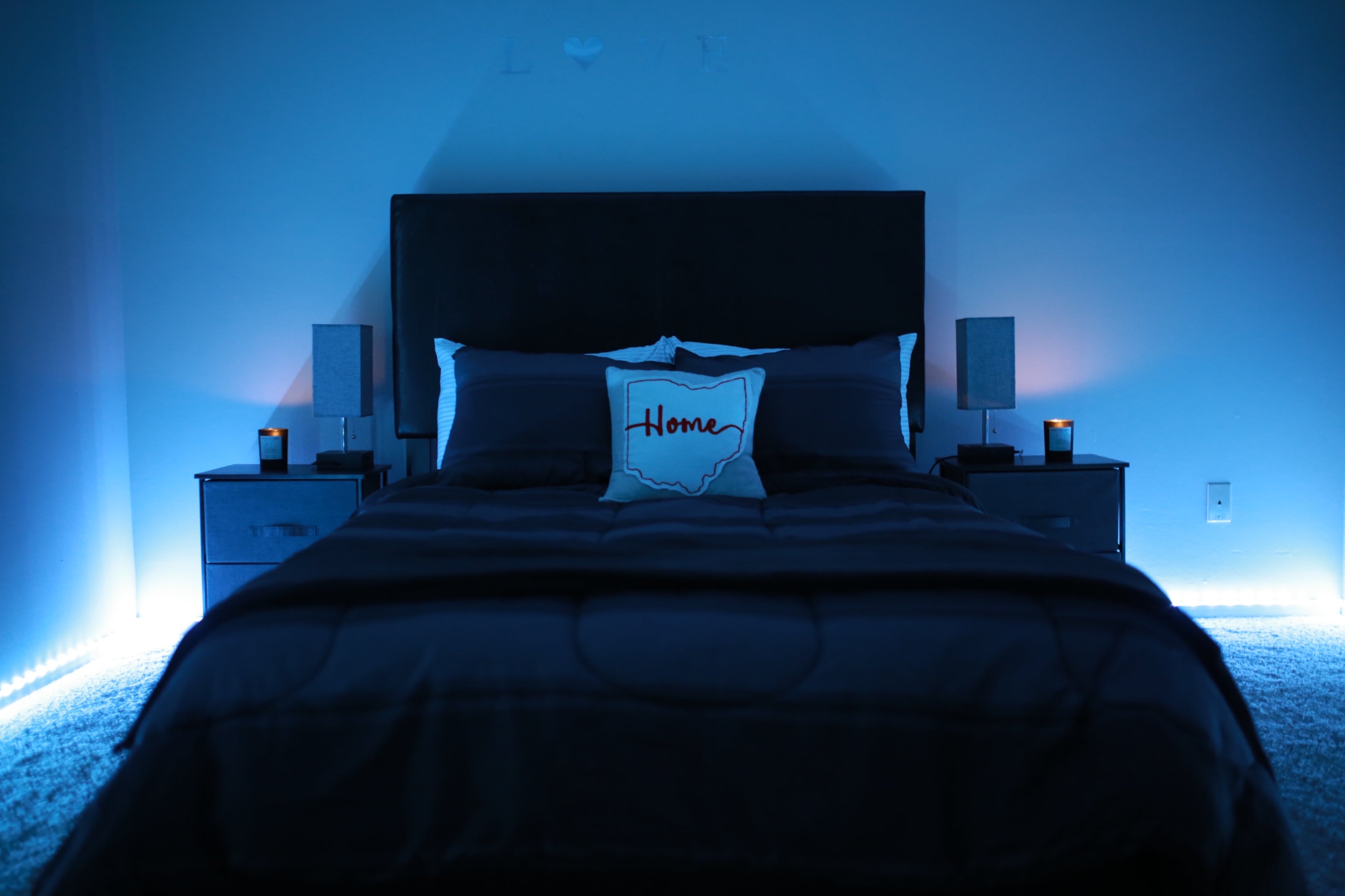 A neatly made bed with blue lighting features a decorative pillow and candles on nightstands.