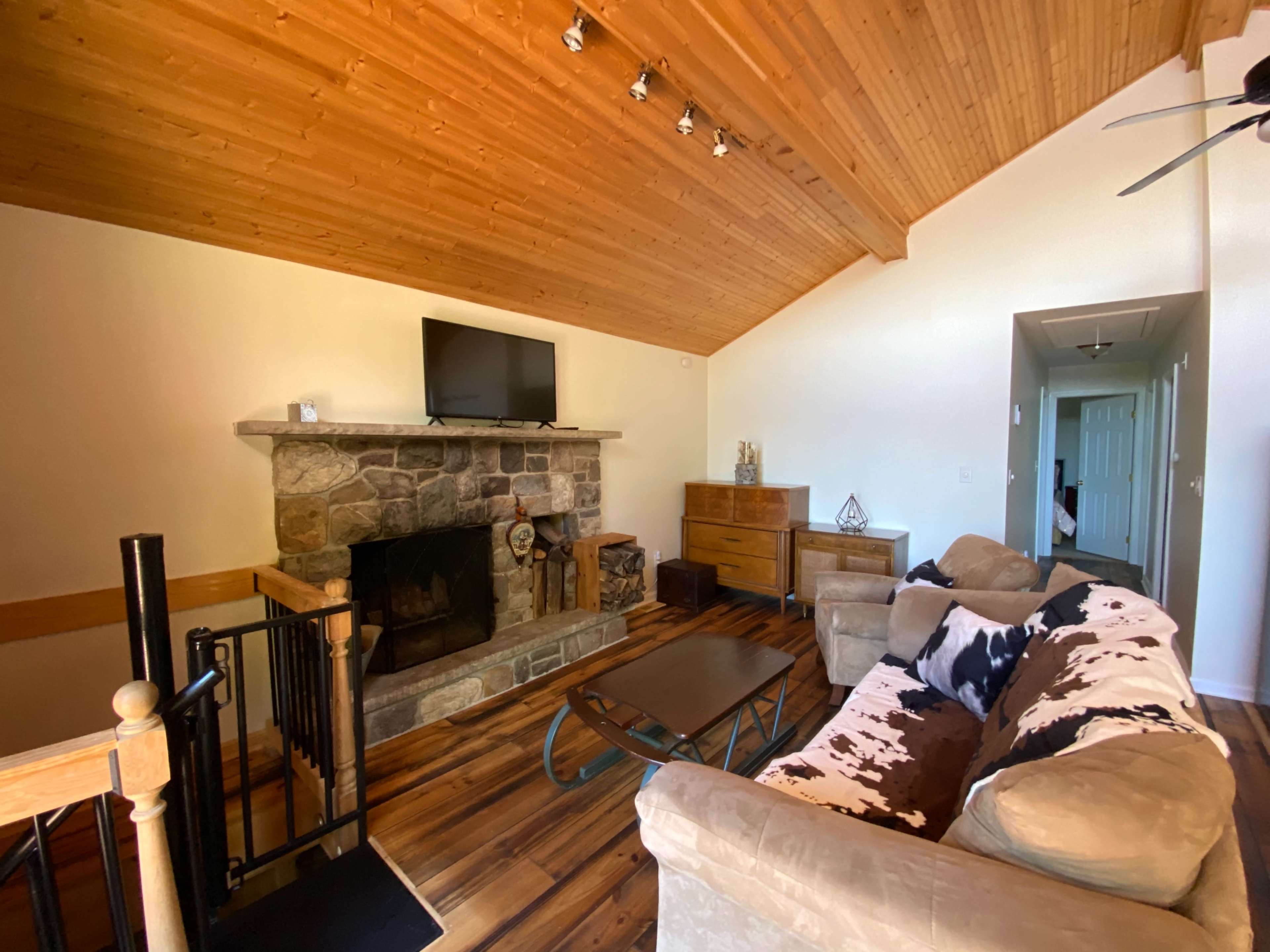 The image shows a living room with a stone fireplace, wooden ceiling, and a sofa facing a coffee table.