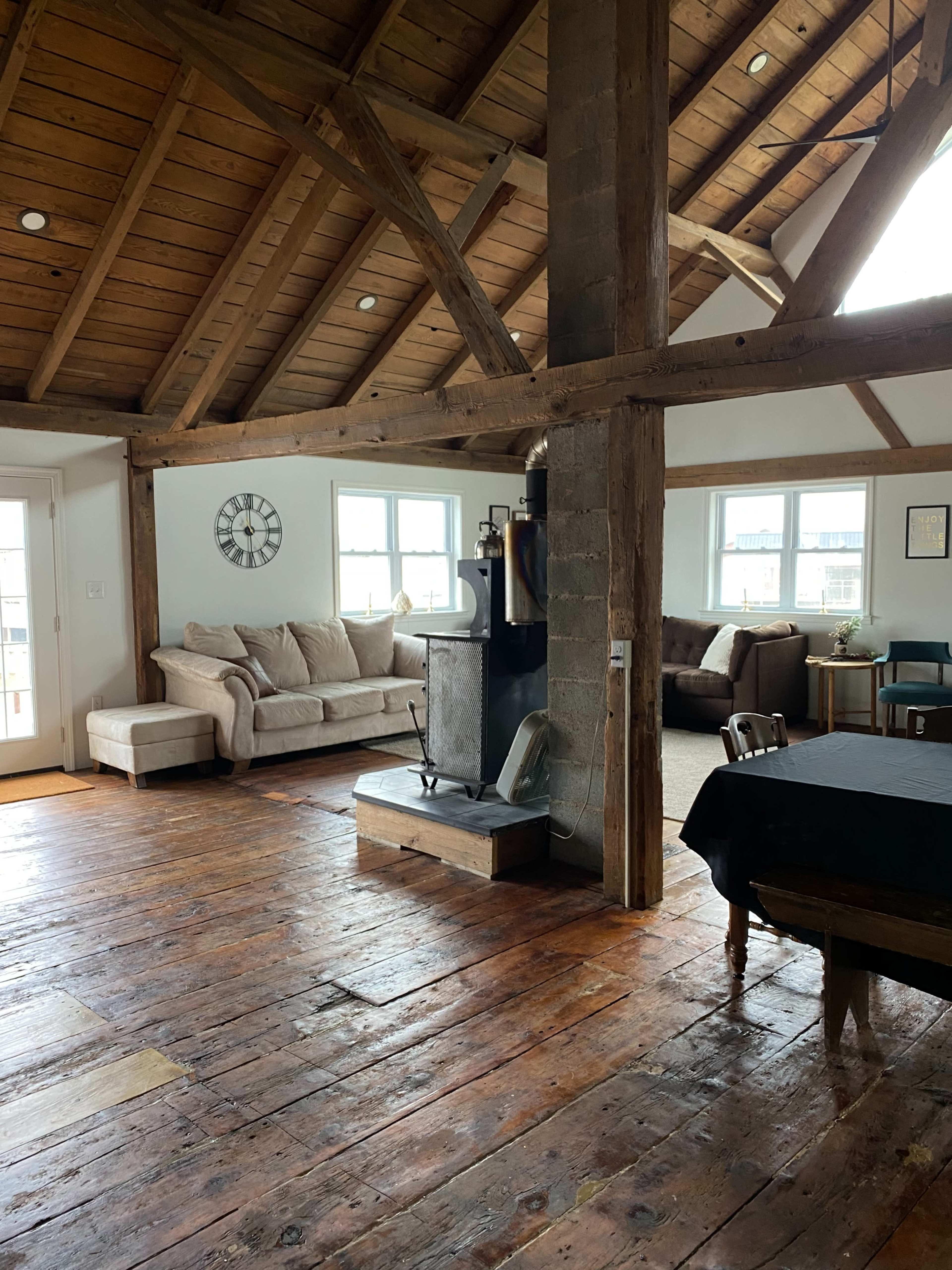 A spacious, rustic room featuring exposed wooden beams, a cozy seating area with a large couch, and a wooden dining table.