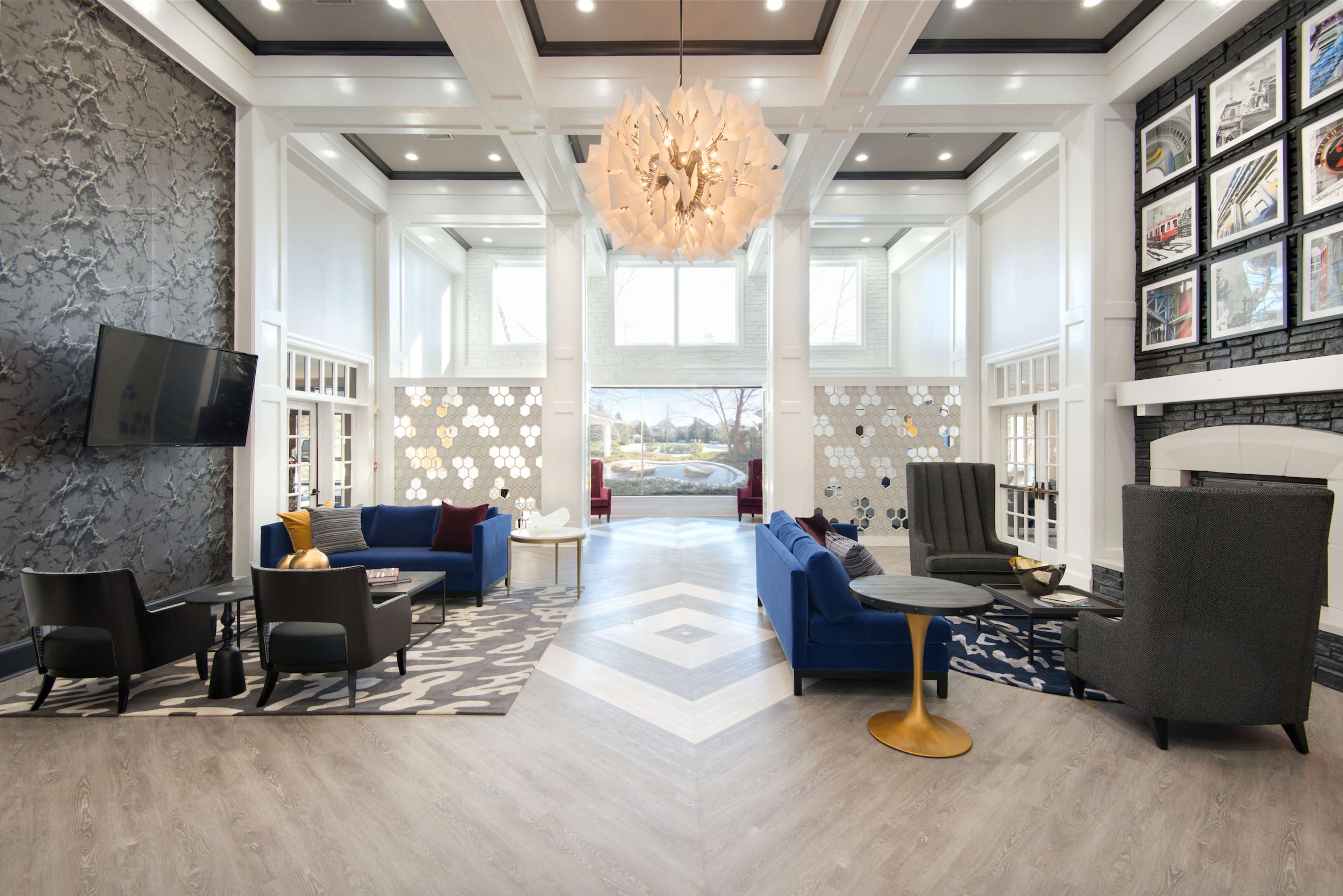 The image shows a modern lobby area with seating arrangements, a large light fixture, and artwork displayed on the walls.